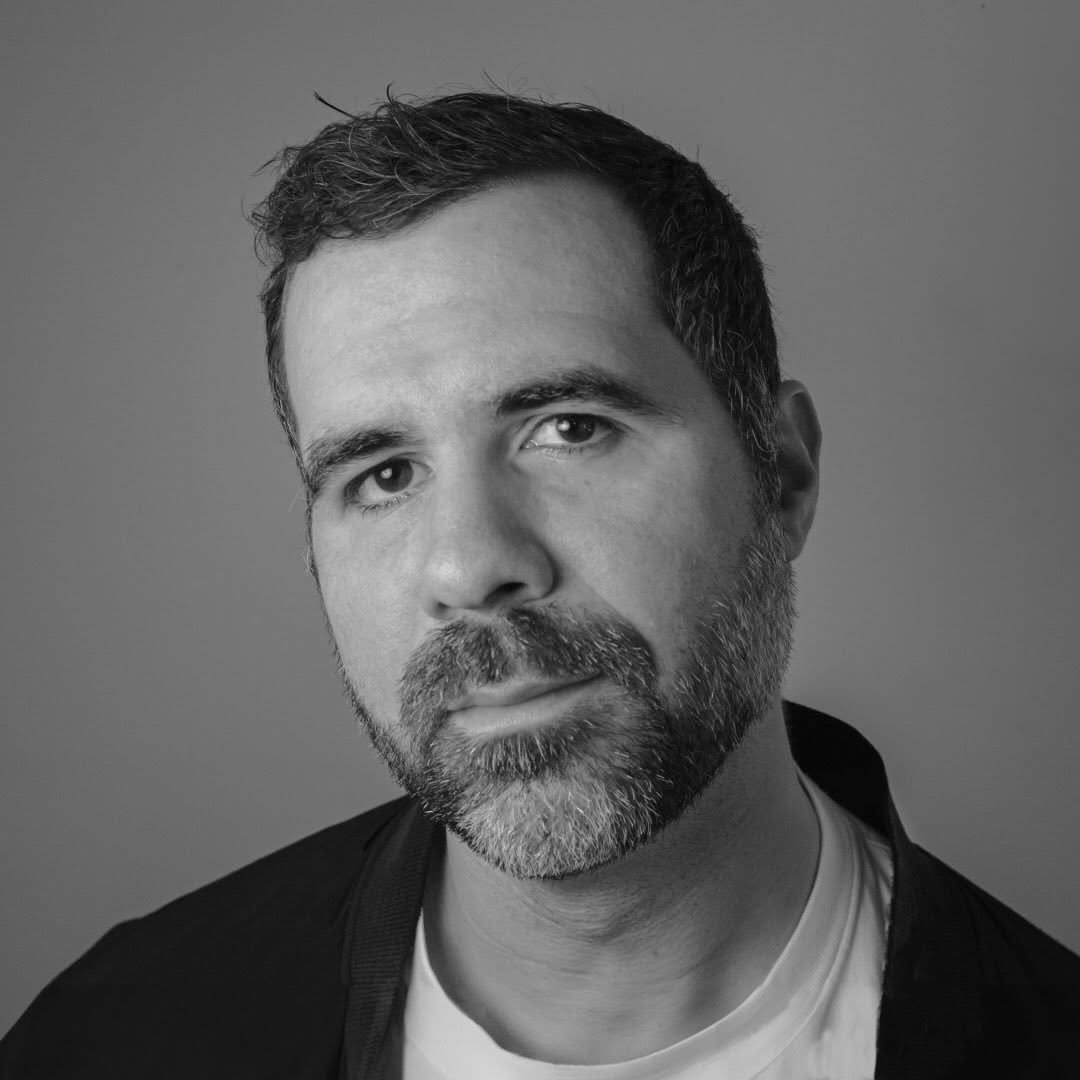 Black-and-white close-up portrait of a bearded man wearing a jacket and T-shirt.
