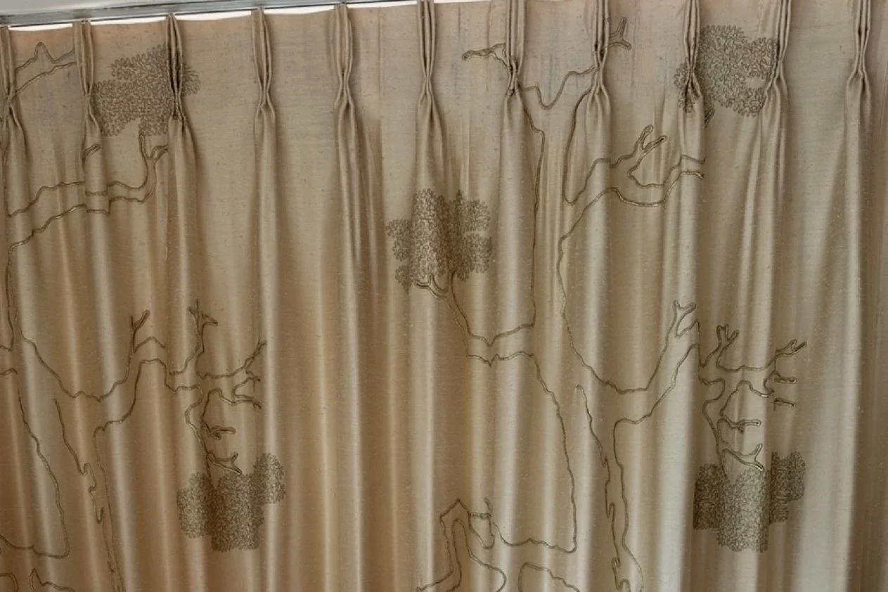 Gold drapery with dark embroidered trees and pinch pleats, hung in the upstairs primary bedroom