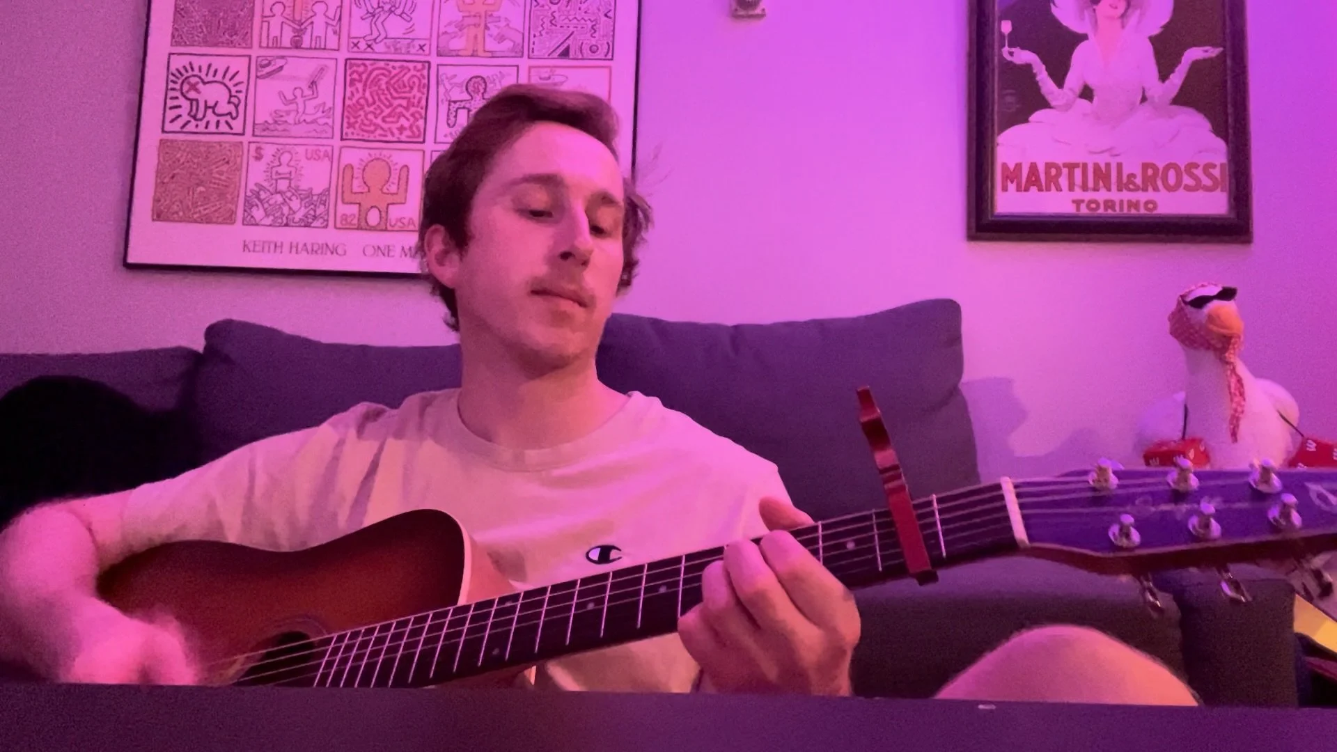 Person playing an acoustic guitar on a couch under pink lighting