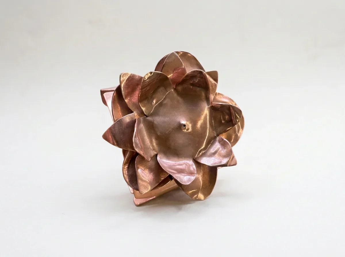 Close-up of a sculptural copper metal flower with layered petals on a white background
