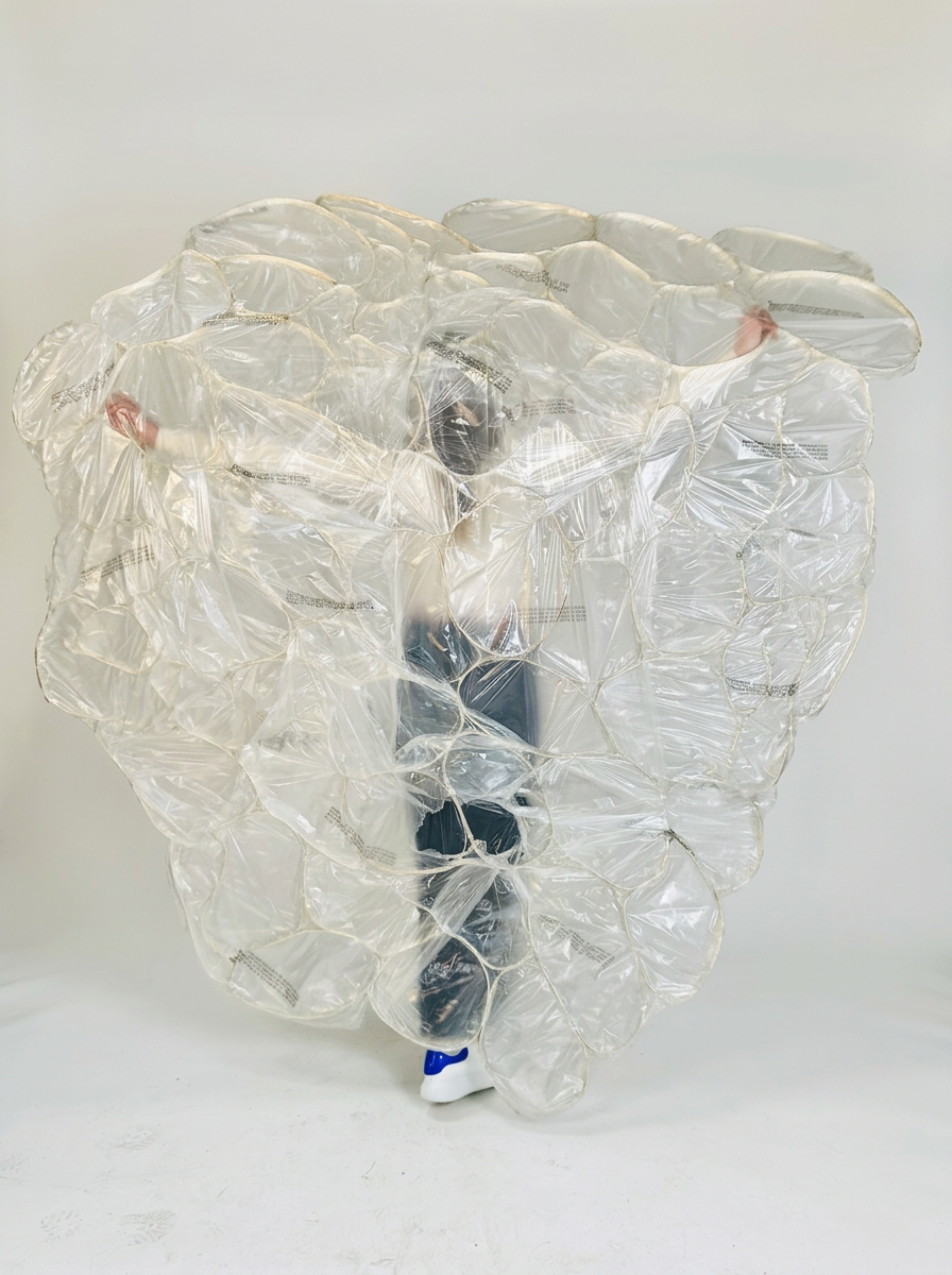 Person wearing an oversized transparent inflatable bubble suit with blue-and-white shoes visible underneath