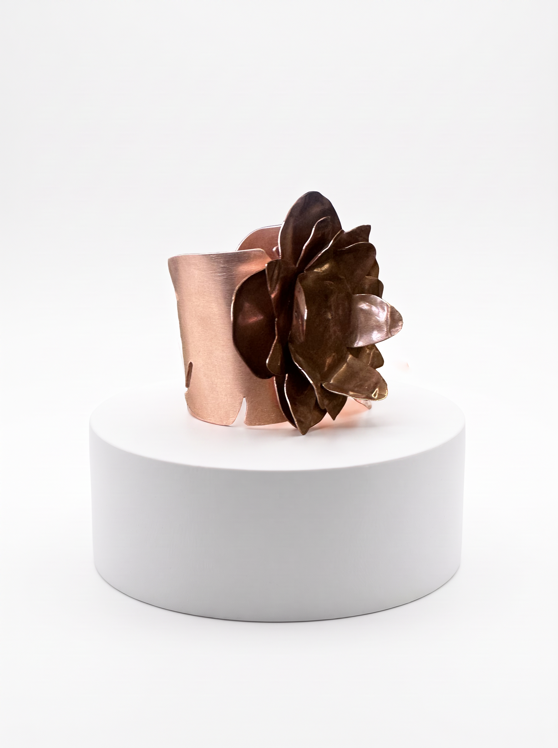 Copper-tone floral cuff bracelet displayed on a white pedestal