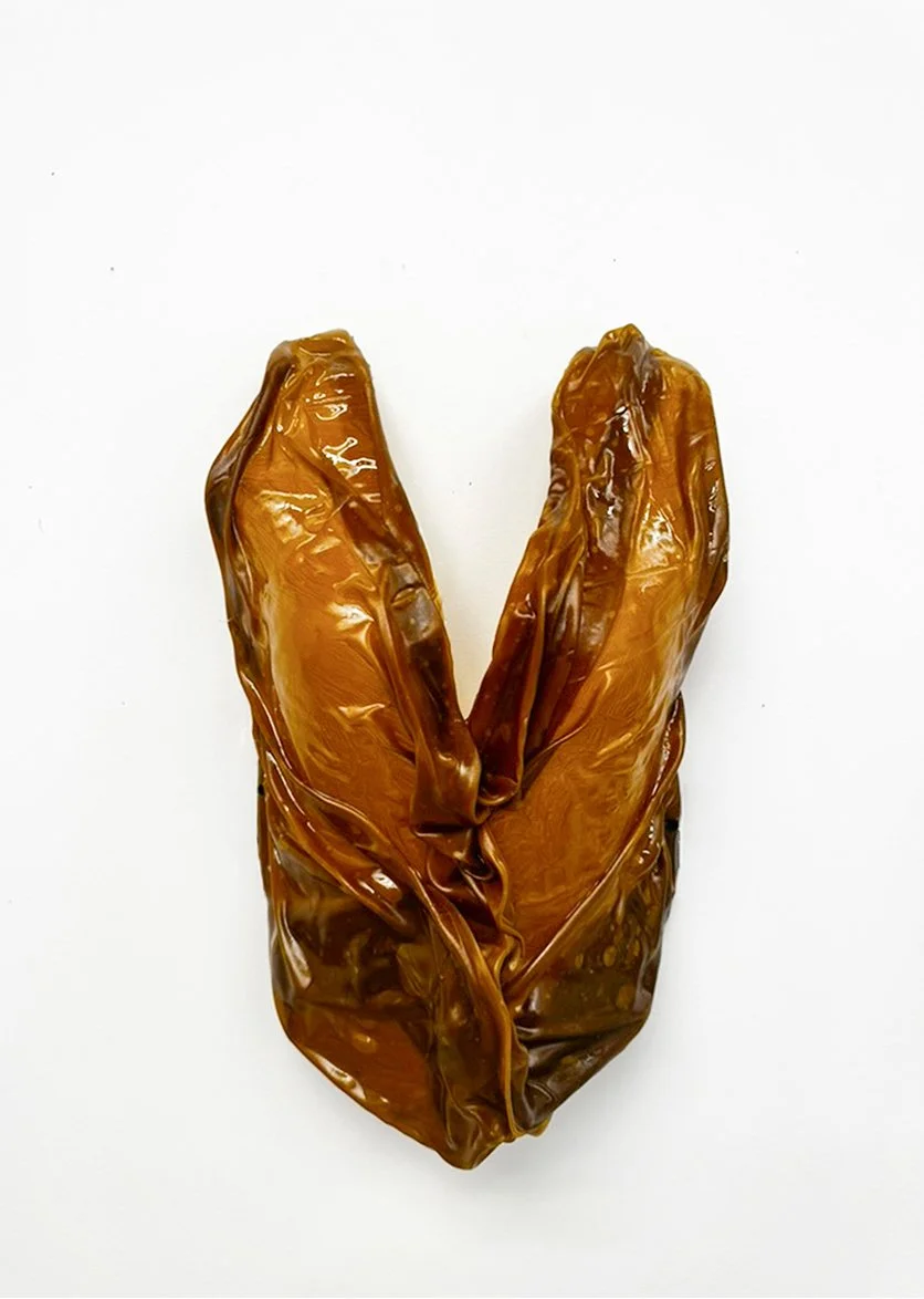 Close-up of a glossy amber-colored sculptural object resembling folded leaves on a white background