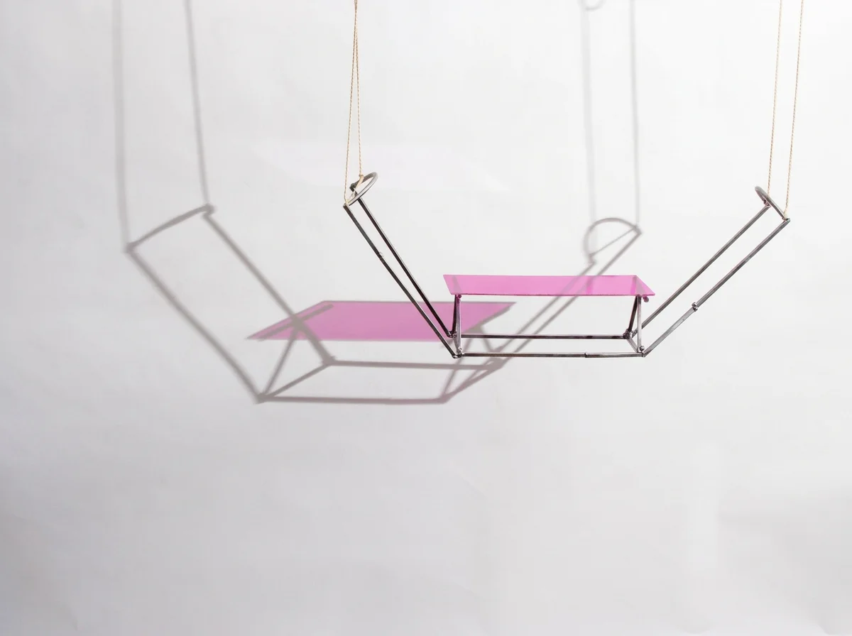 Abstract pink and chrome geometric hanging sculpture casting shadows on a white wall