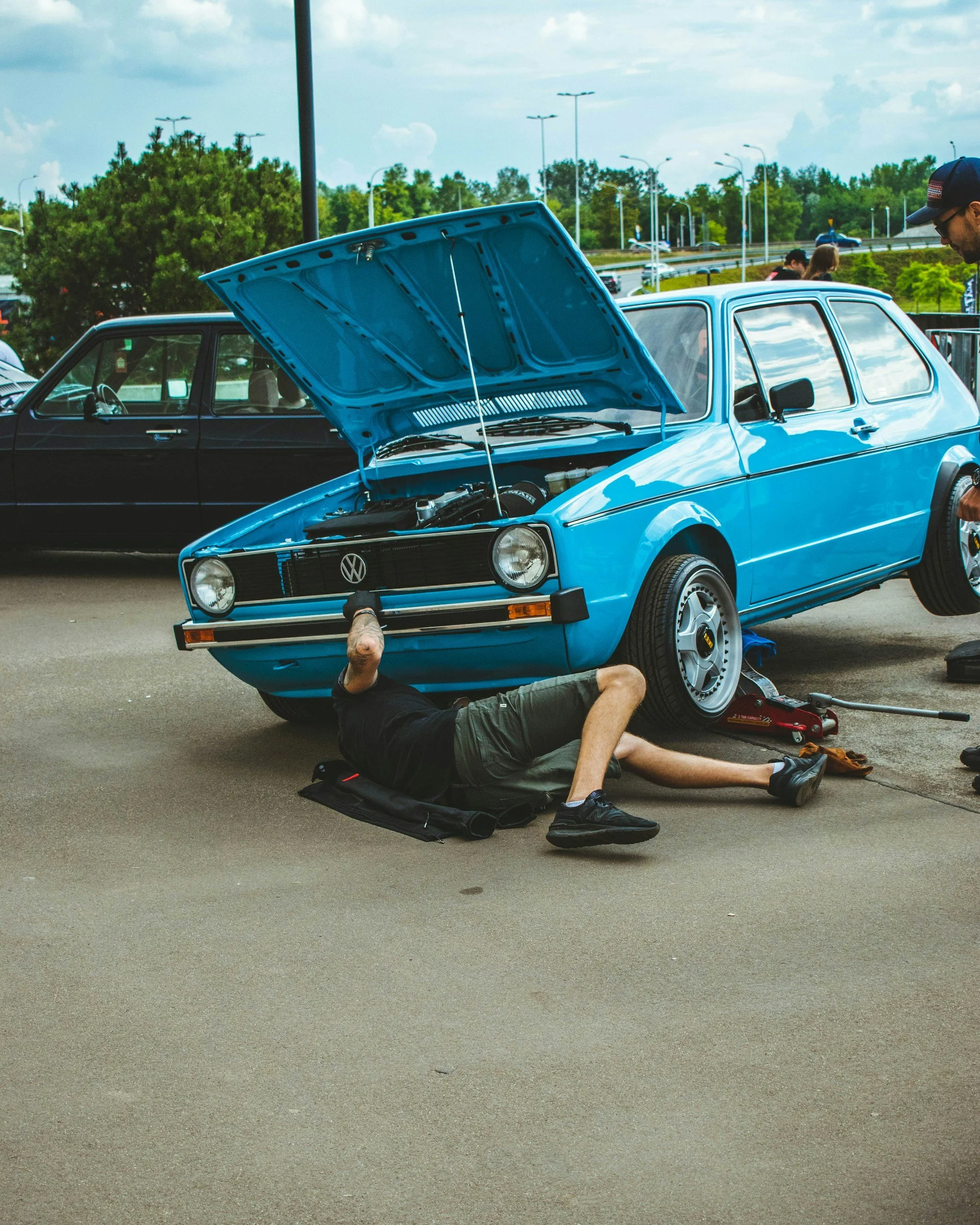 Mechanic repairing a bright blue vintage Volkswagen with the hood open at an outdoor car show