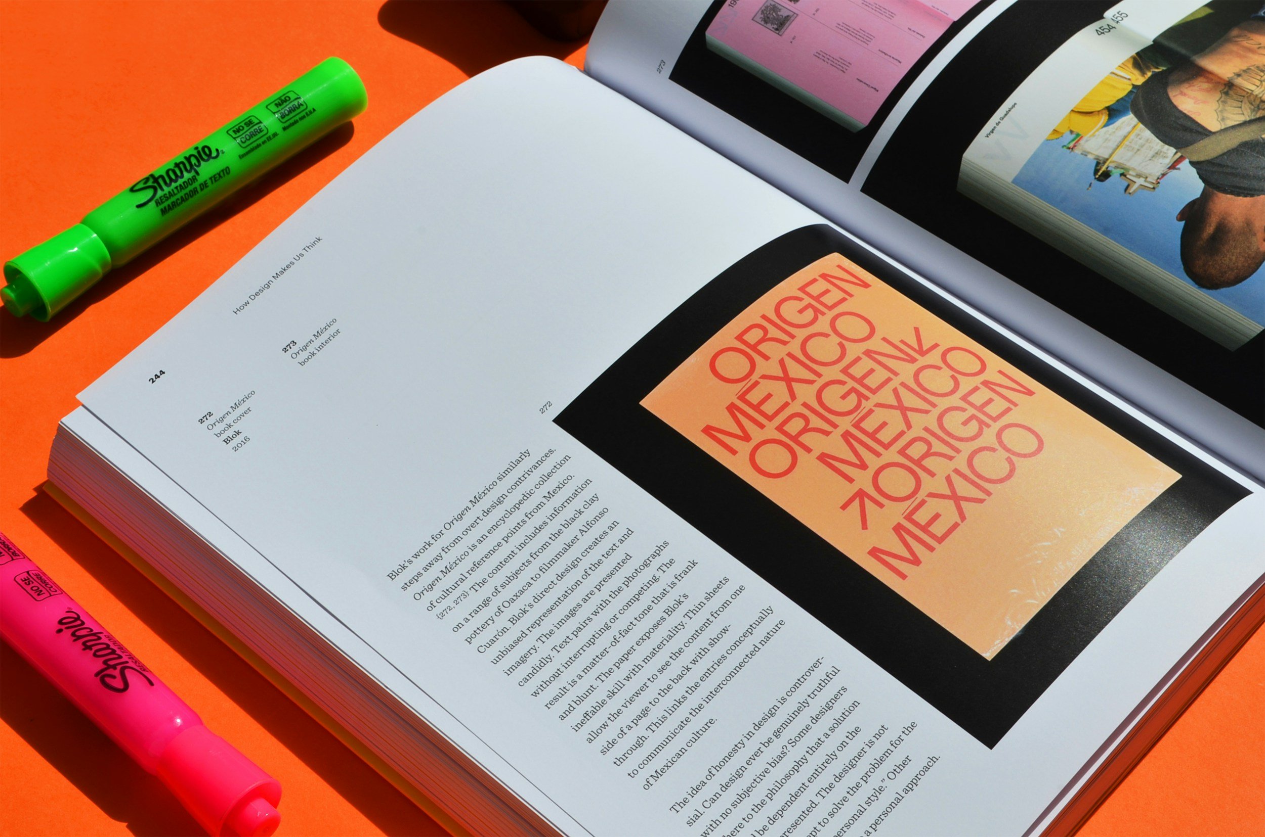 Libros y revistas de diseño abiertos sobre una mesa naranja, acompañados de marcadores fluorescentes verde y rosa.