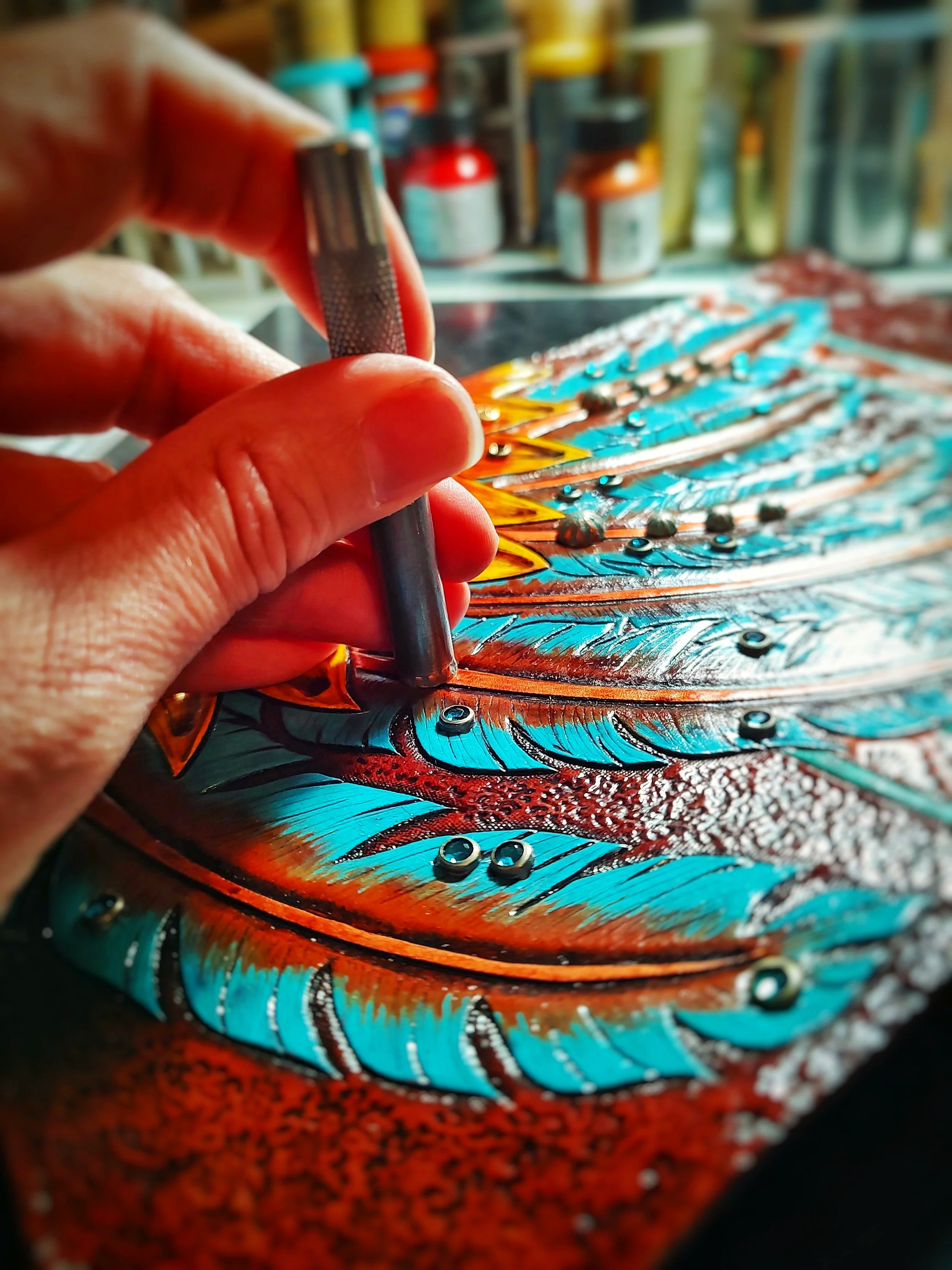Someone setting rhinestones on a tooled and painted piece of leather