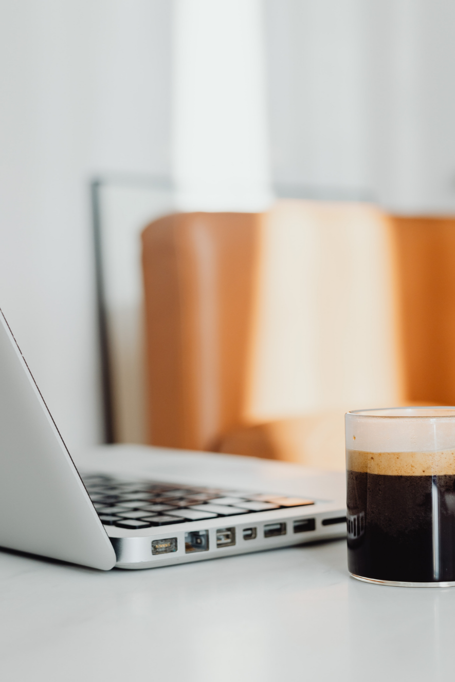 Open silver laptop beside a glass of black coffee on a white desk