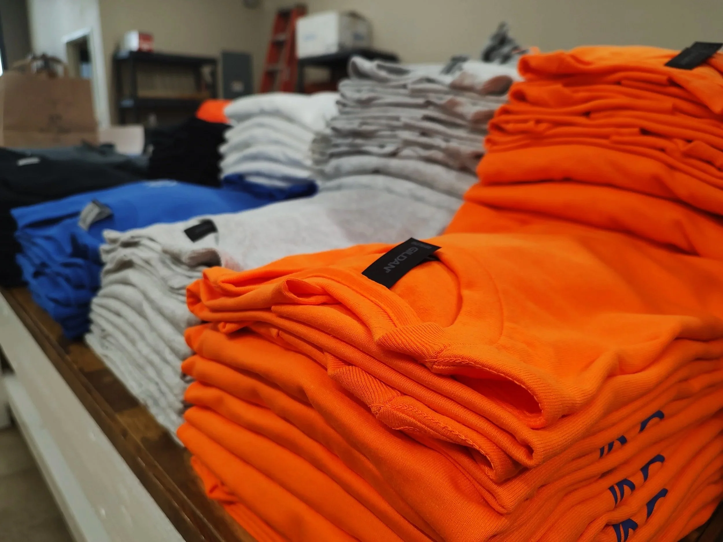 Stacks of folded orange, white, gray, blue, and black T-shirts on a table