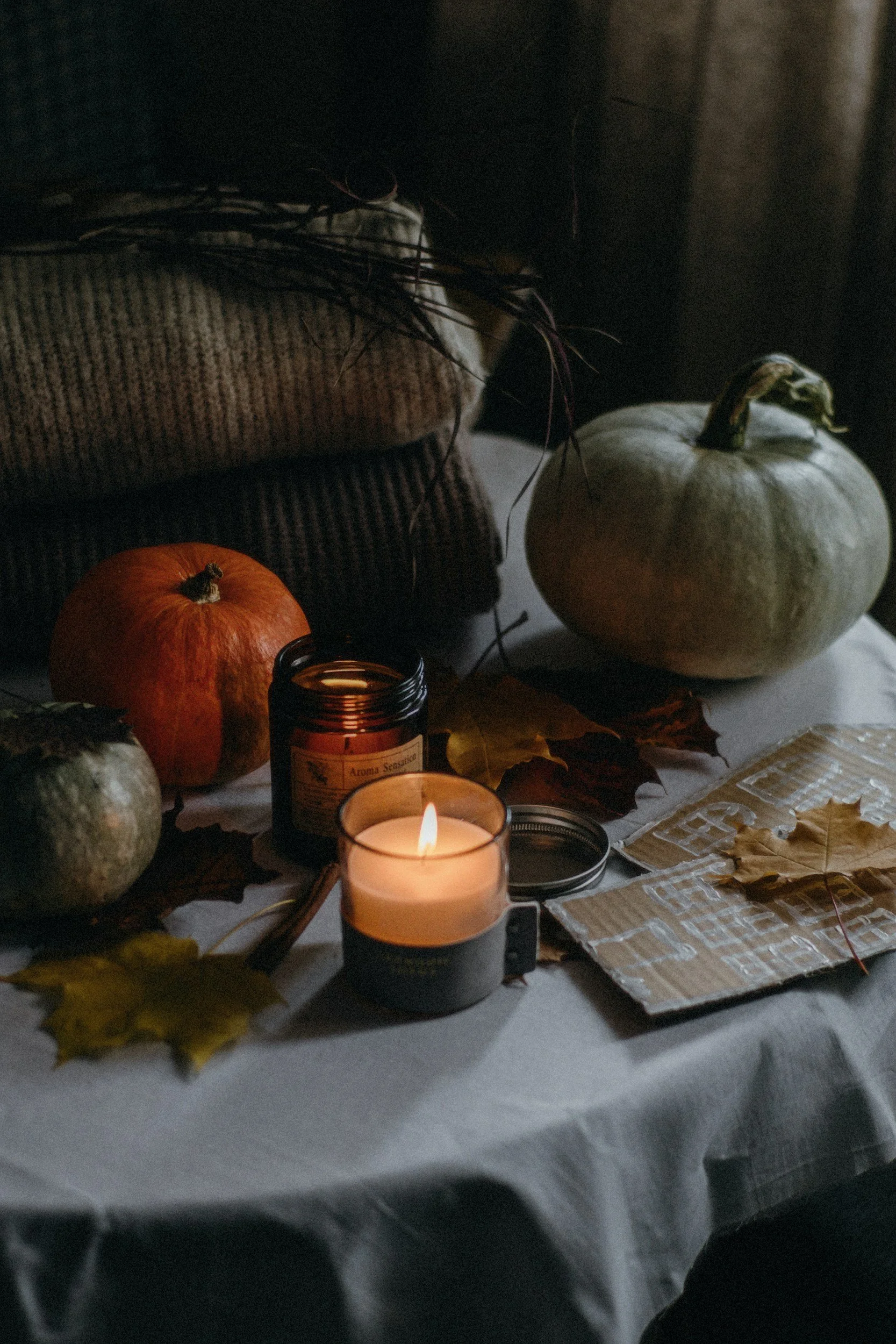 Lit candles and pumpkins styled for fall on a linen table