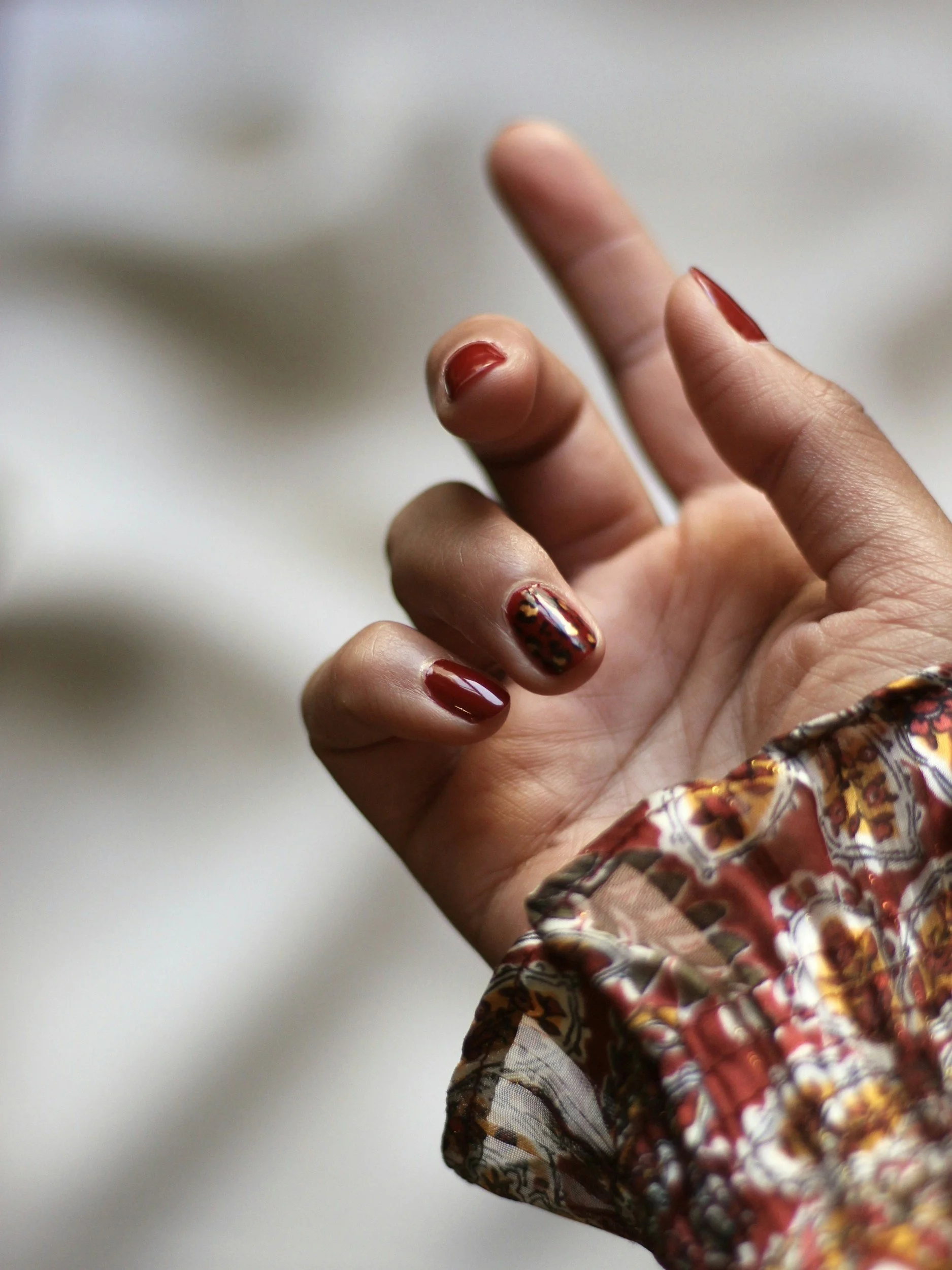 Hand with deep burgundy almond nails against a neutral background