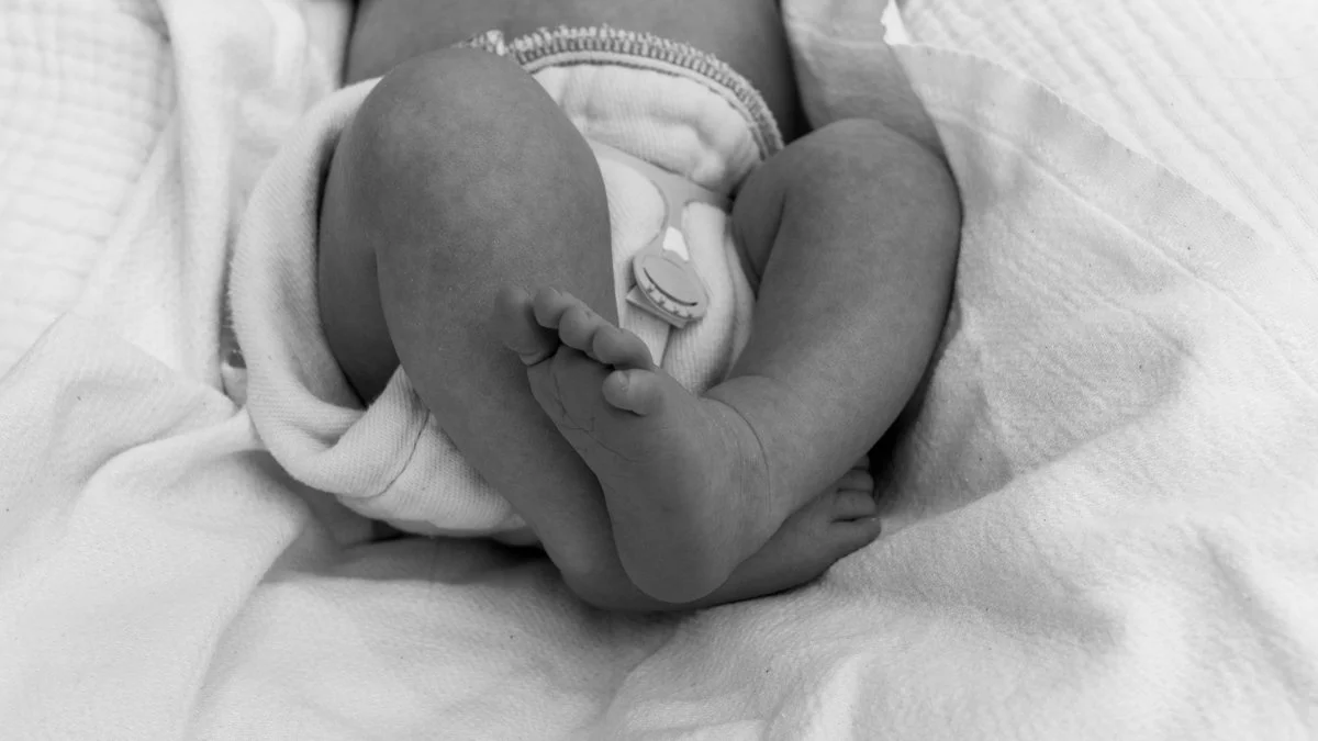 Black-and-white close-up of a newborn baby's crossed legs and feet resting on a soft blanket