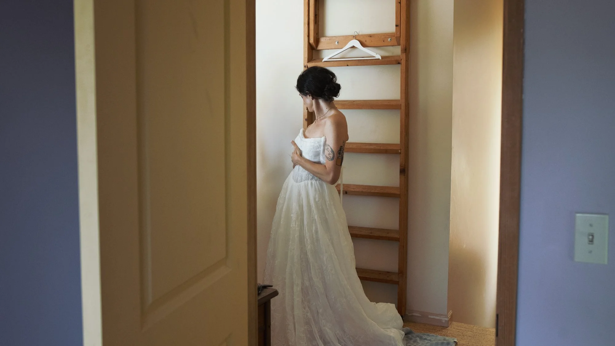 Woman in a white wedding dress standing in a room beside a wooden clothing rack