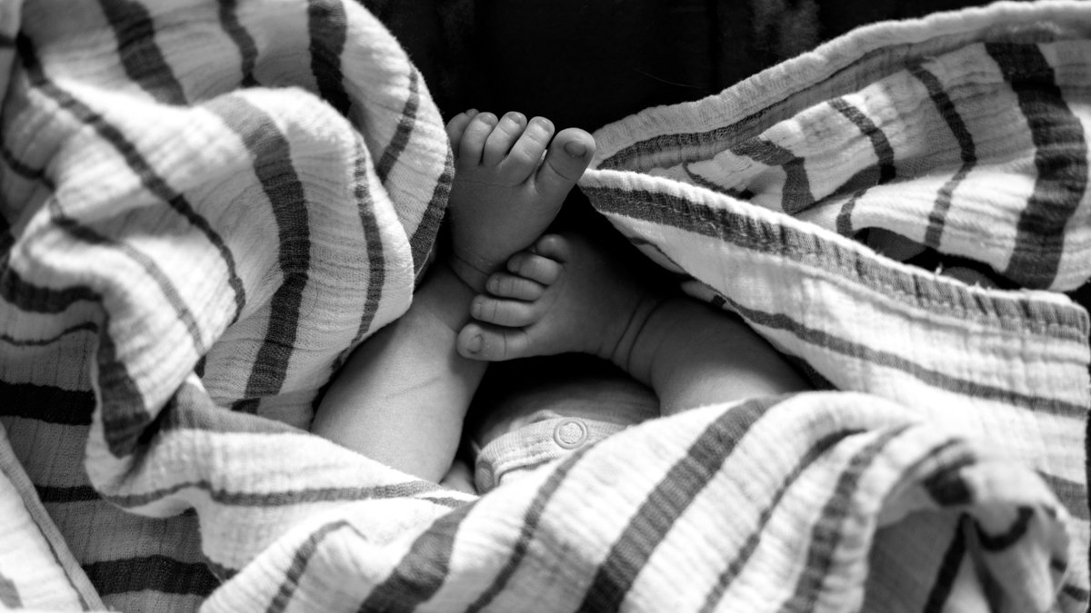 Black-and-white close-up of a baby's feet and legs nestled in a striped blanket