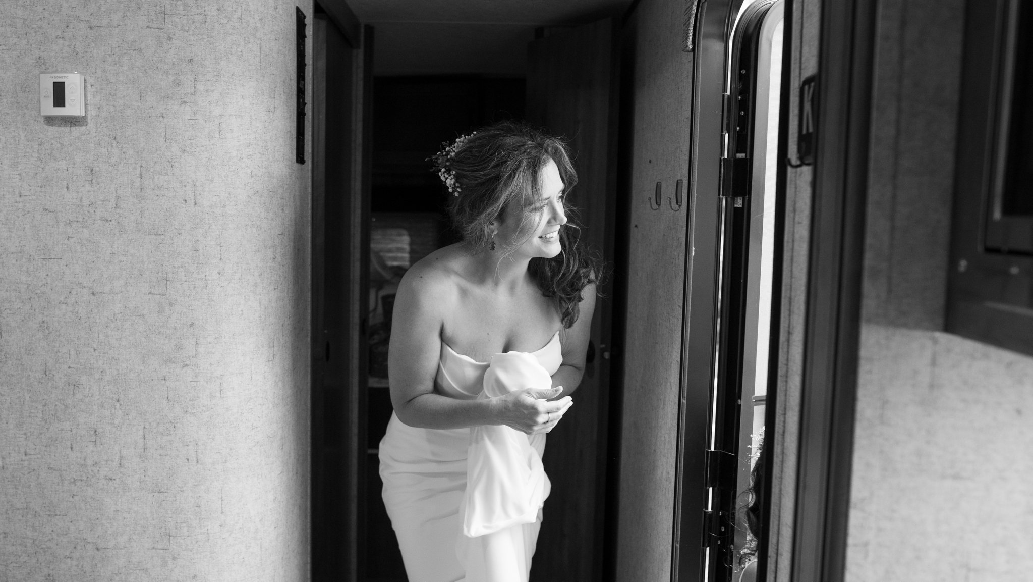 Black-and-white photo of a smiling bride in a strapless wedding dress standing in a doorway