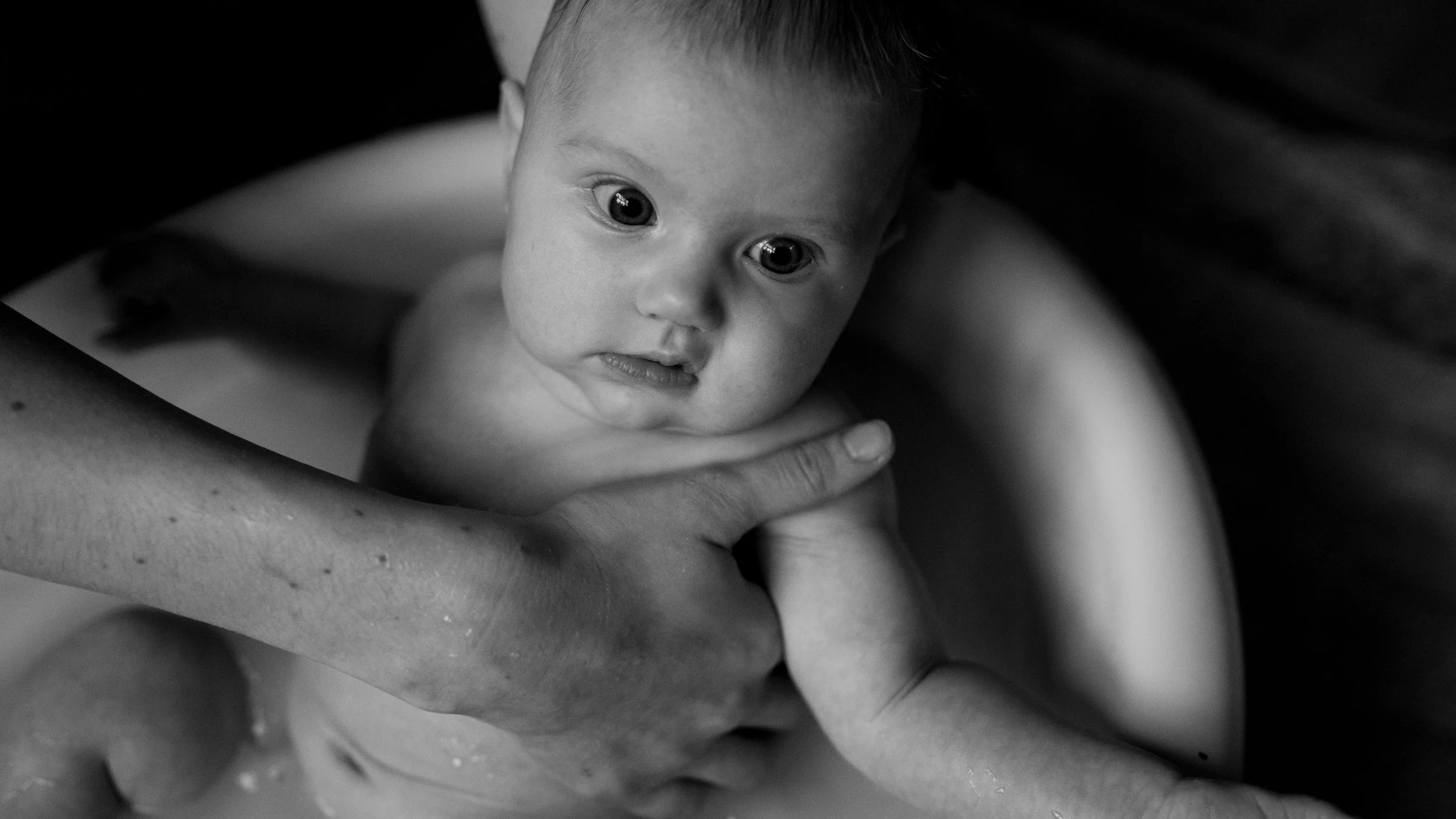 Black-and-white close-up of a newborn baby supported by an adult's hands.