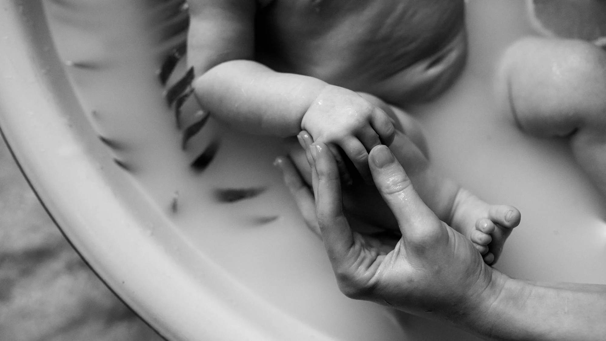 Black-and-white close-up of an adult gently holding a newborn baby's hand and foot.