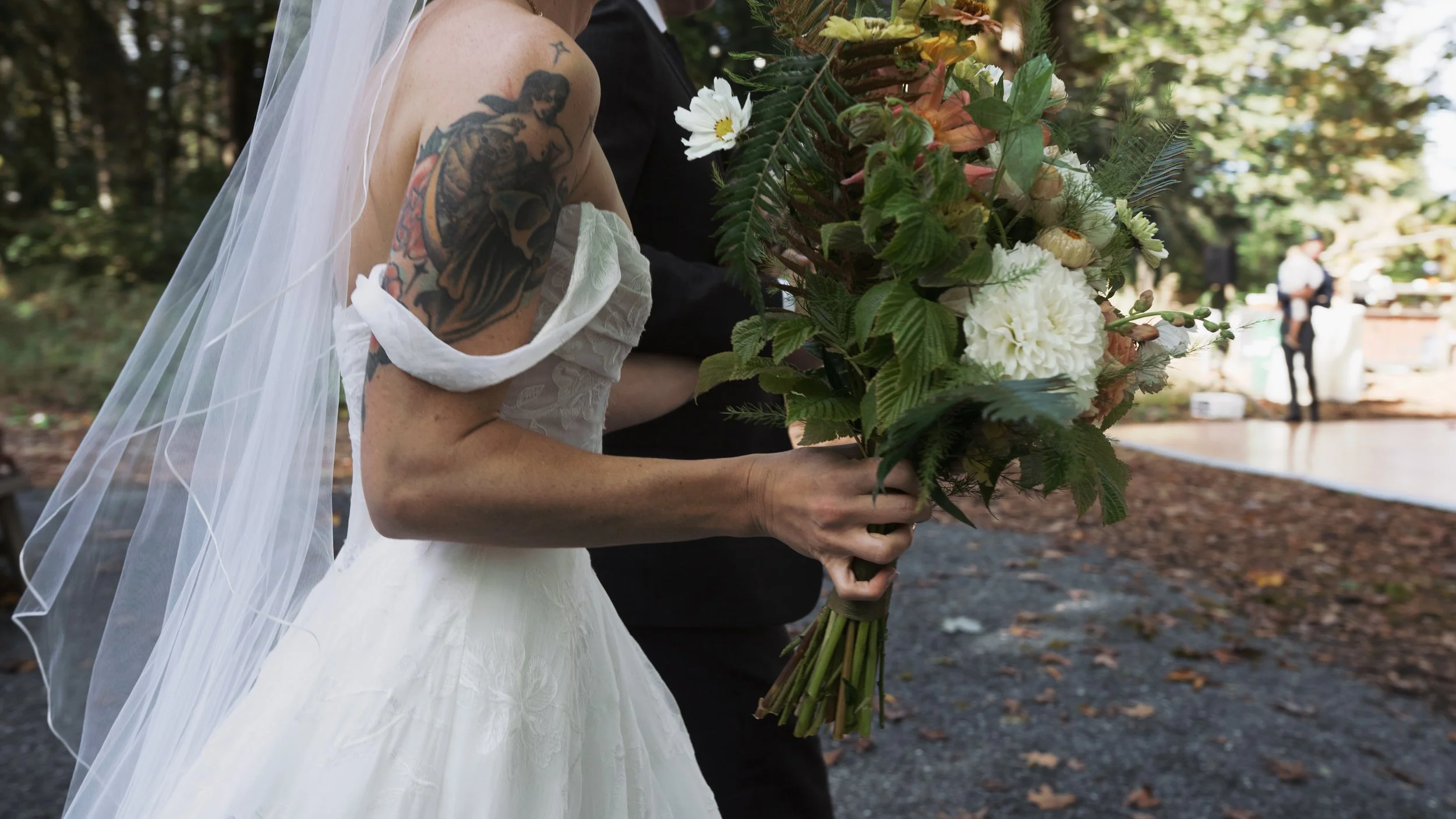 Bride in a white wedding dress and veil holding a rustic floral bouquet outdoors