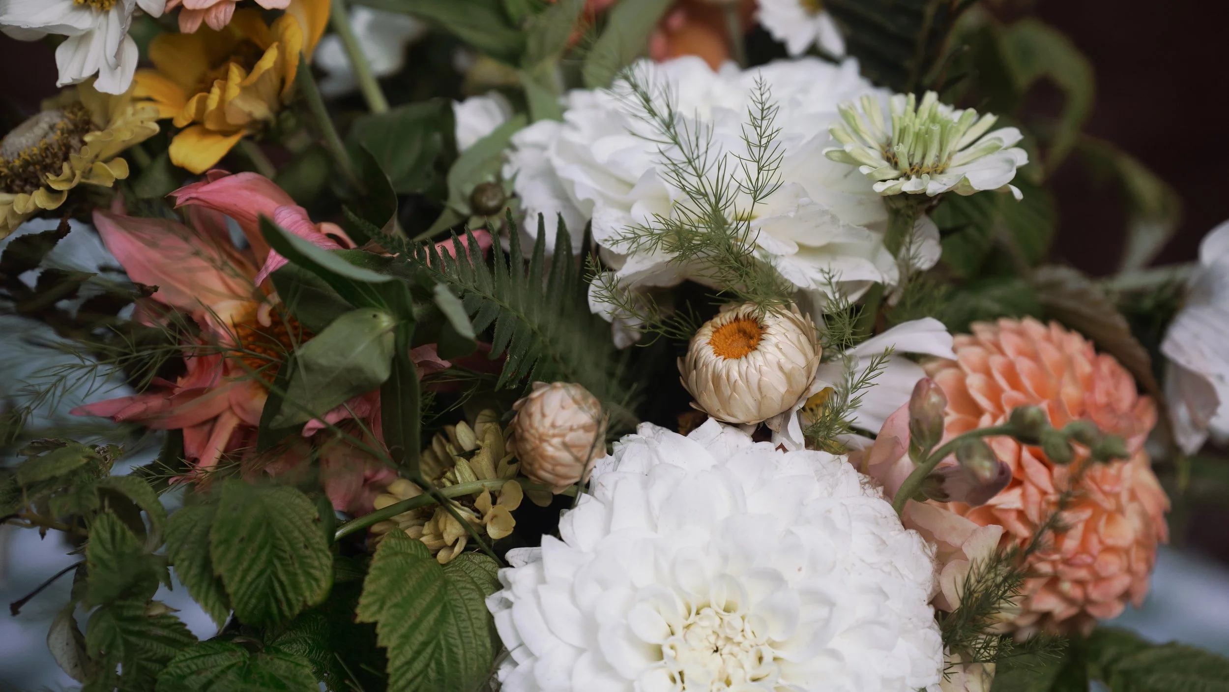 Close-up of a lush mixed flower arrangement with white, pink, yellow, and peach blooms, dried flowers, and green foliage