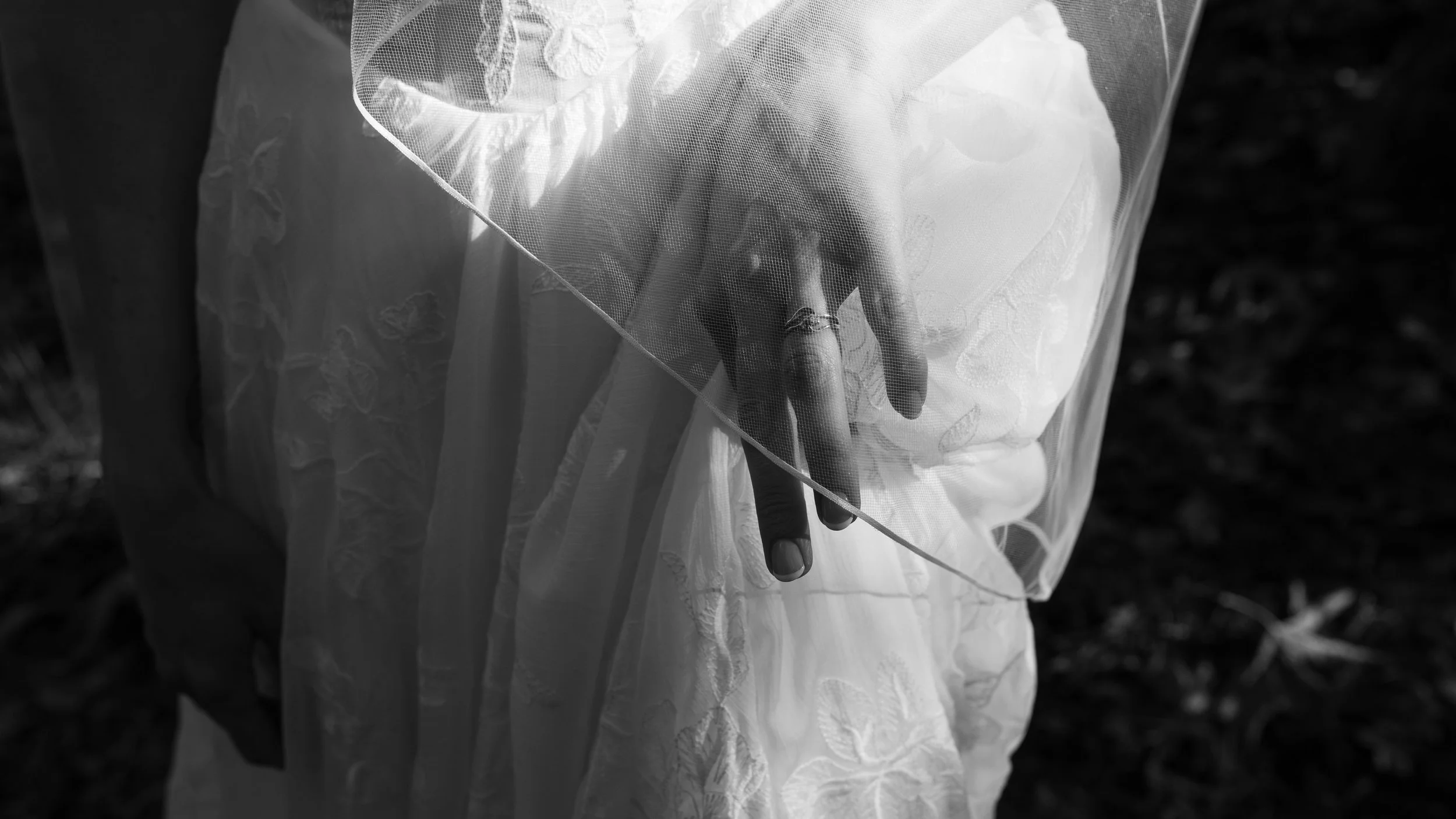 Black-and-white close-up of a bride's hand holding a sheer embroidered wedding veil.