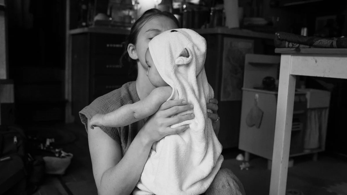 Black-and-white photo of a mother holding a baby wrapped in a towel at home