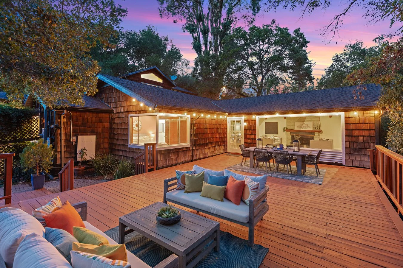 Inviting backyard deck with outdoor sofas, dining area, string lights, and a shingle-sided home at sunset