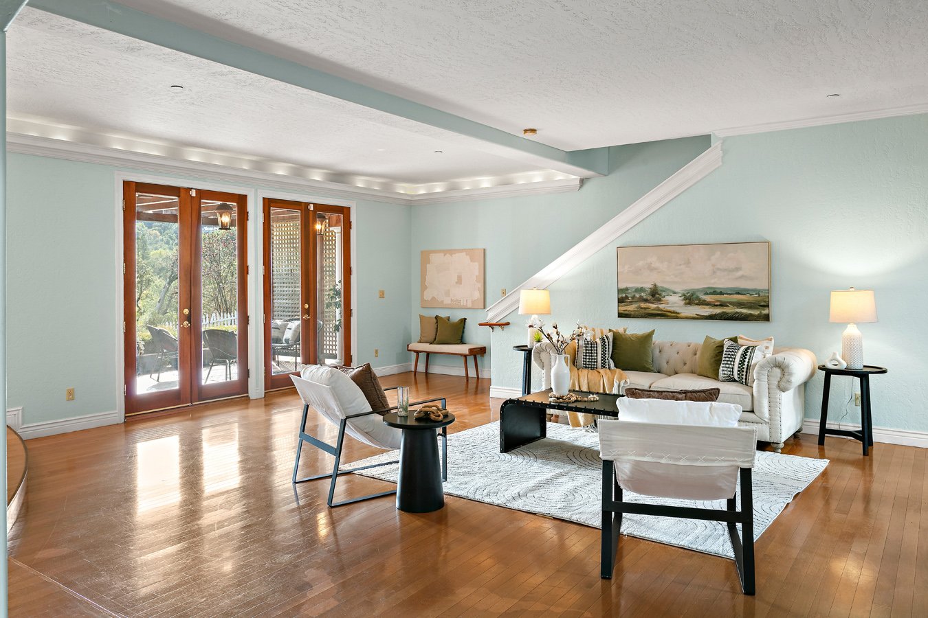 Bright living room with hardwood floors, pale blue walls, white sofa, armchairs, coffee table, and French doors opening to a patio