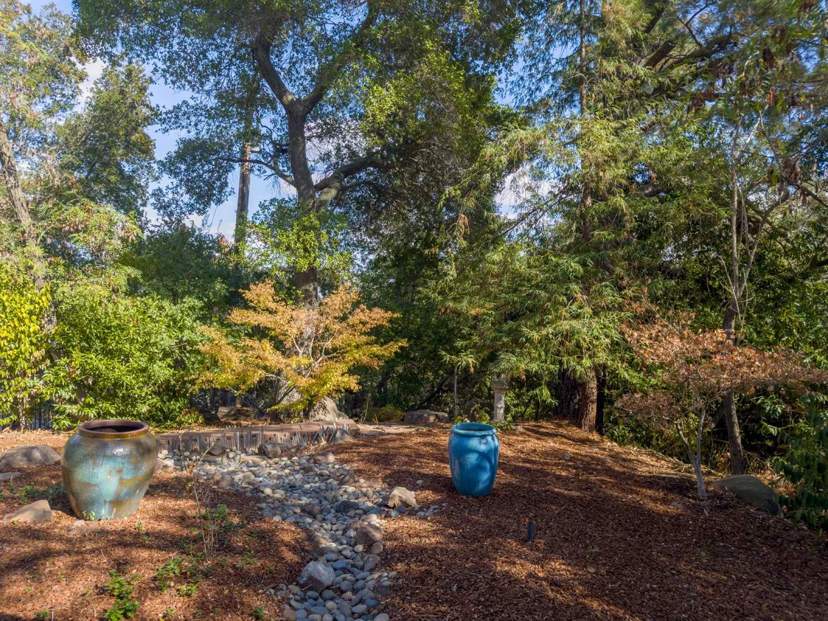 Landscaped garden with large ceramic pots, a stone-lined dry creek bed, and mature trees