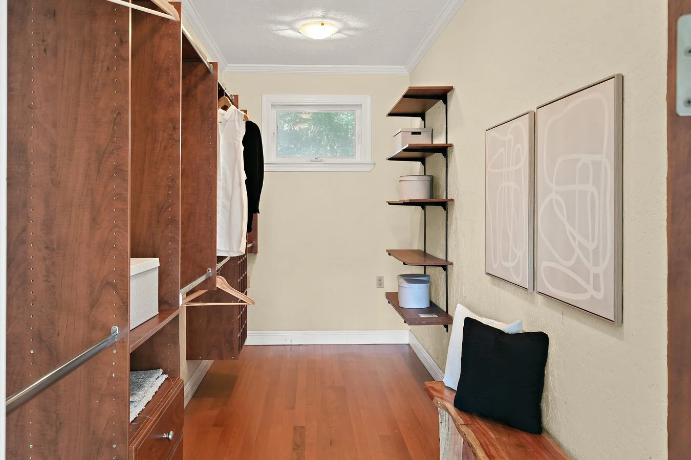 Walk-in closet with built-in wooden wardrobes, open shelving, hanging clothes, bench seating, and hardwood flooring