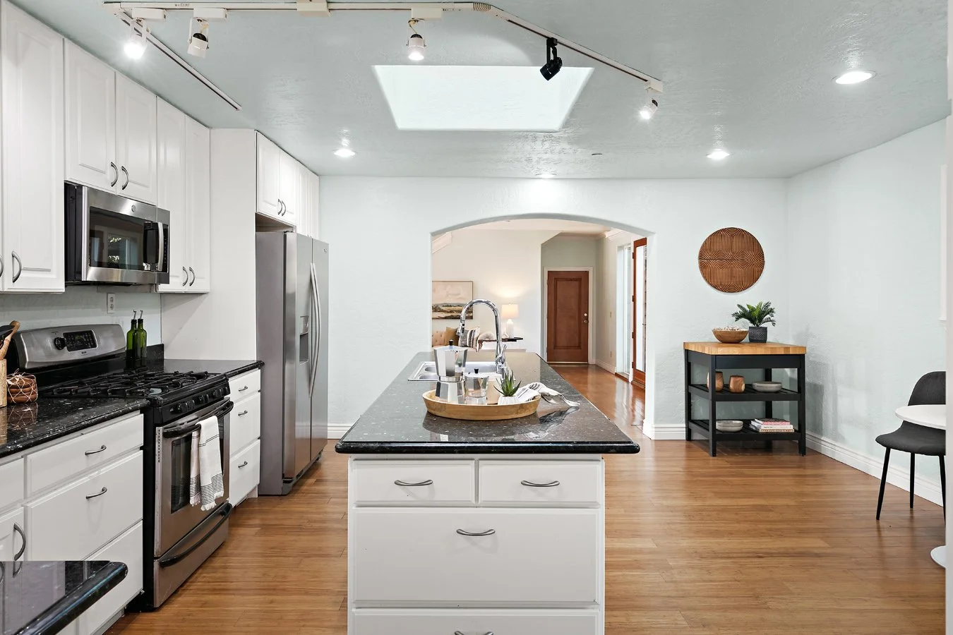 Bright modern white kitchen with central island, black granite countertops, stainless steel appliances, and adjoining dining area