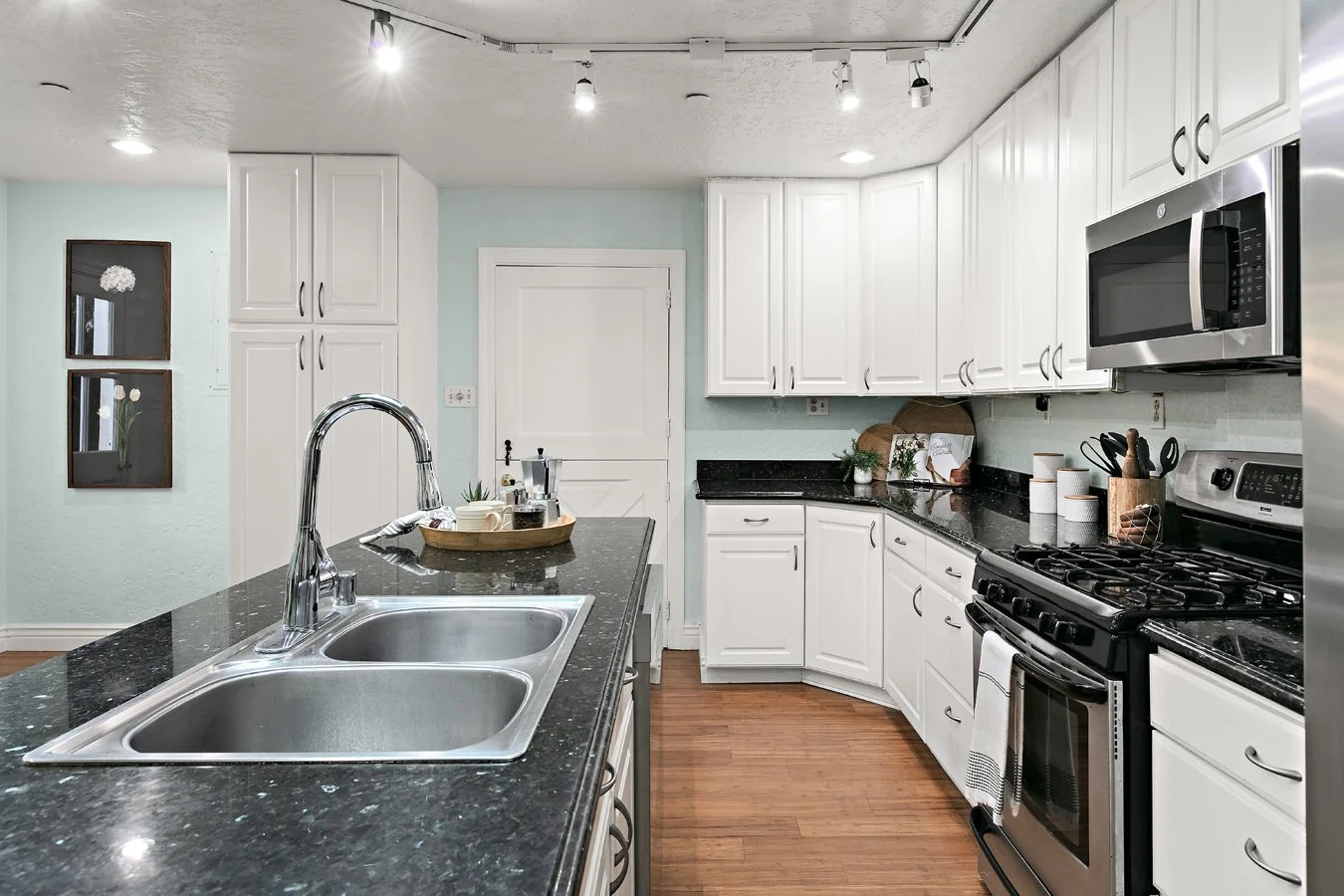 Bright modern kitchen with white cabinets, black granite countertops, double-basin sink, stainless steel appliances, and central island.