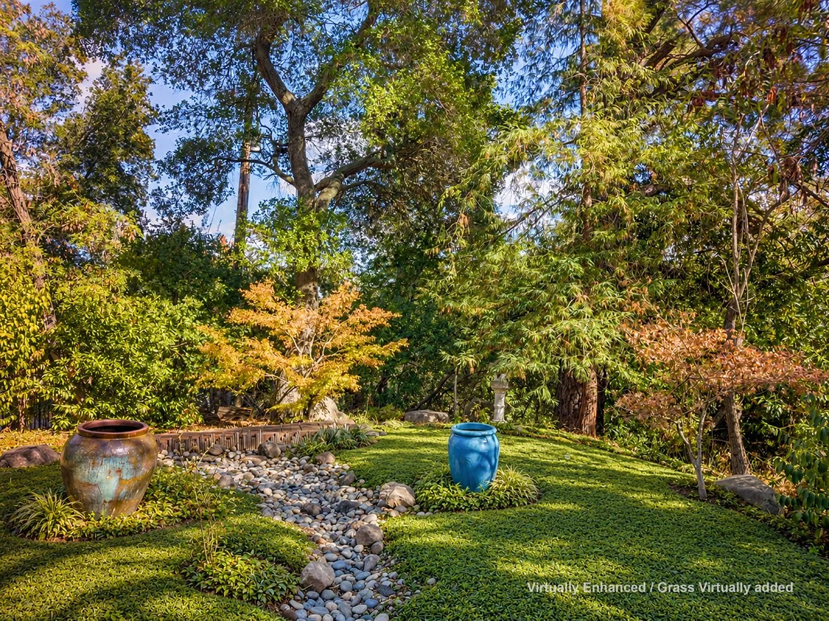 Lush landscaped garden with trees, ground cover, a dry creek bed, rocks, and two colorful ceramic pots