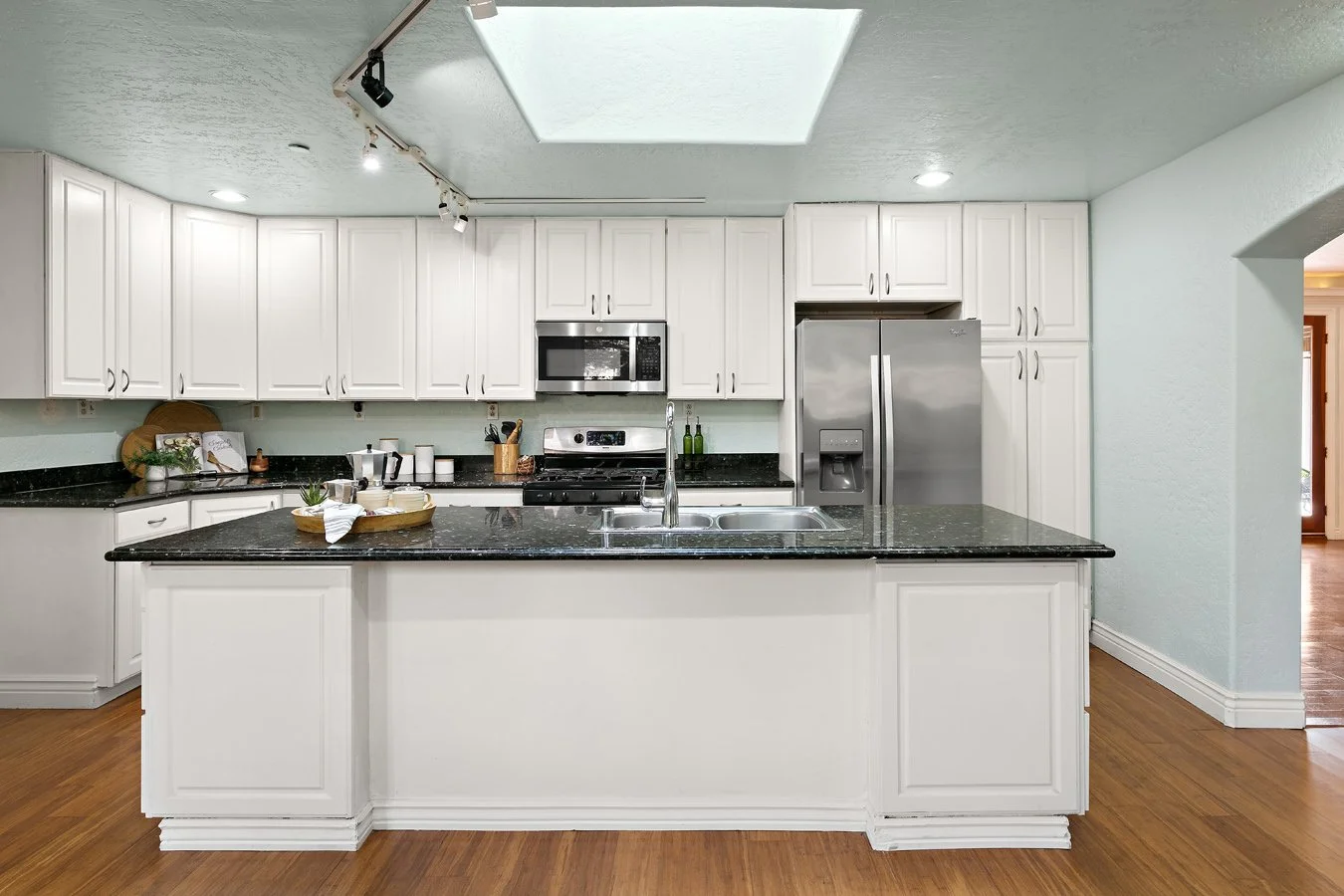 Bright white kitchen with black granite countertops, center island sink, stainless steel appliances, and hardwood floors