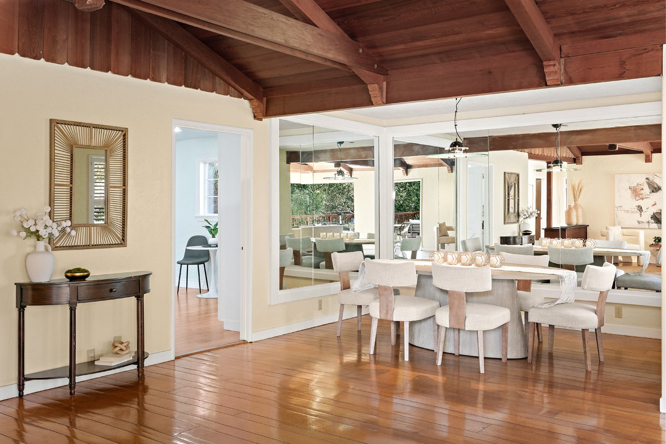 Elegant dining room with exposed wood-beam ceiling, polished hardwood floors, large wall mirrors, and a white dining table surrounded by upholstered chairs.