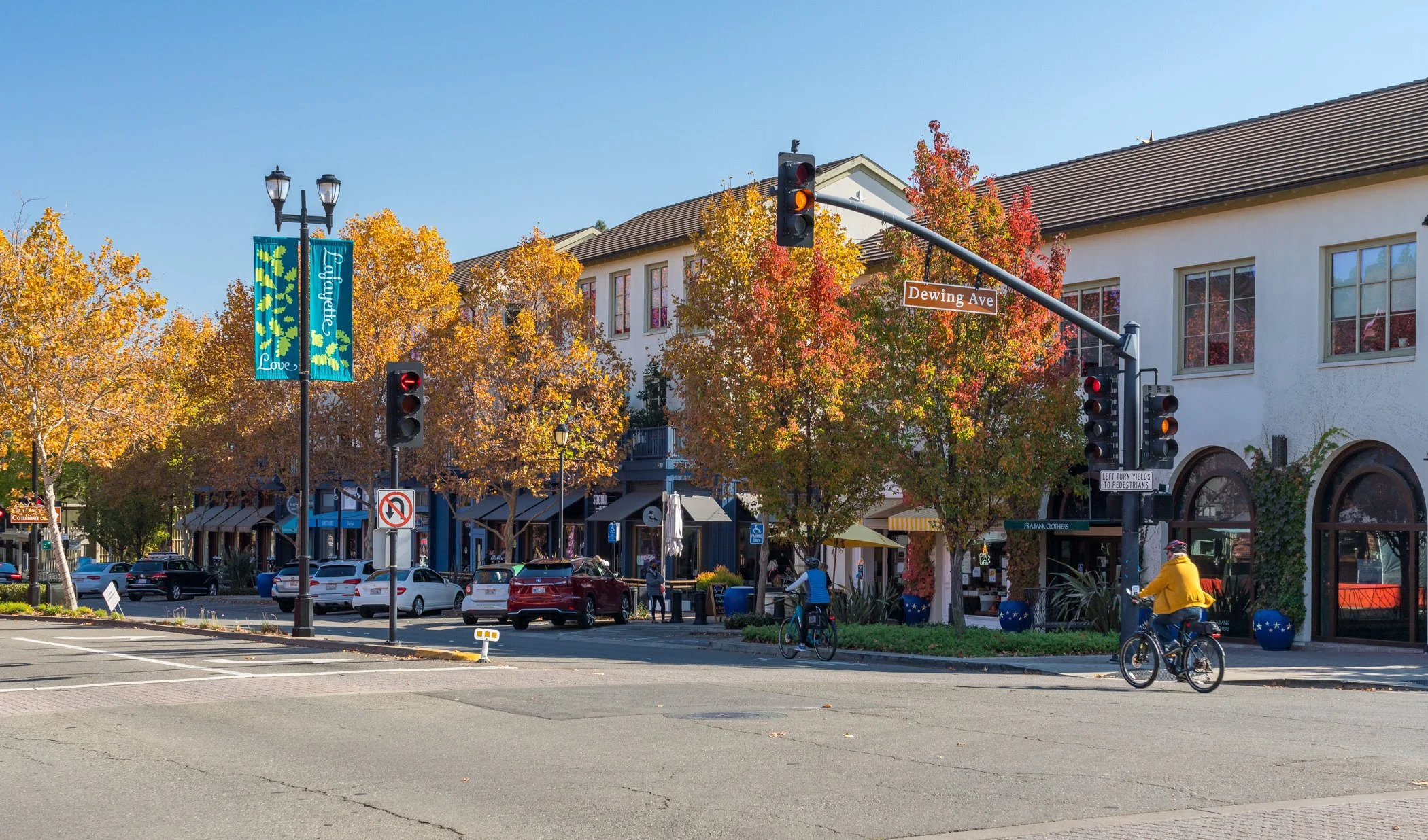 Downtown Lafayette, California, street intersection with Dewing Avenue sign, traffic lights, autumn trees, shops, cars, and cyclists.