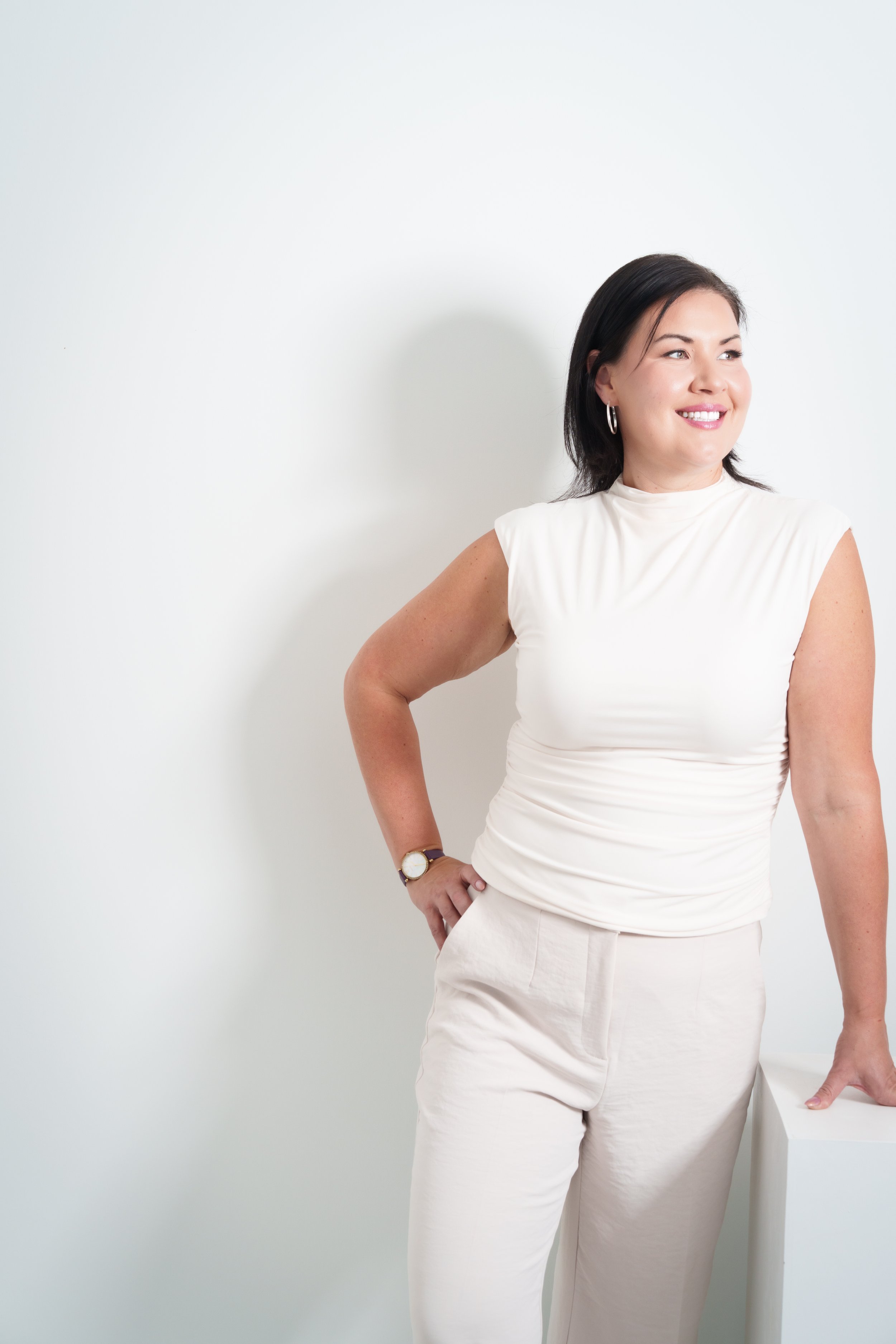 Smiling woman in a white top and pants standing against a light background