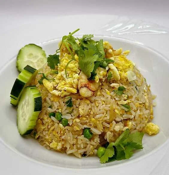 Thai-style fried rice with scrambled egg, shrimp, cilantro, green onions, and cucumber slices on a white plate