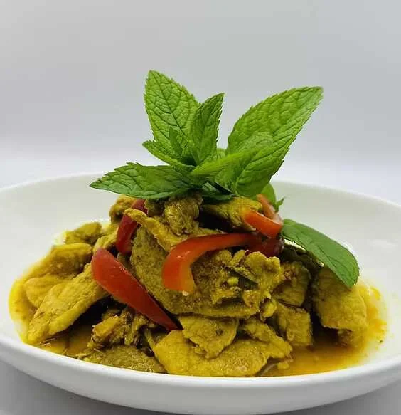 Spicy yellow curry with sliced meat, red peppers, and fresh mint leaves in a white bowl