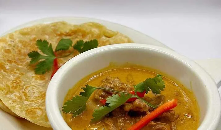 Bowl of yellow curry garnished with cilantro and red chili, served with flatbread