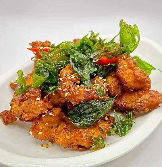 Crispy fried chicken pieces topped with fresh basil, red chilies, and sesame seeds on a white plate