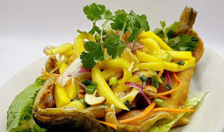 Thai-style green mango salad with crispy fried fish, peanuts, herbs, onions, carrots, and chilies on lettuce