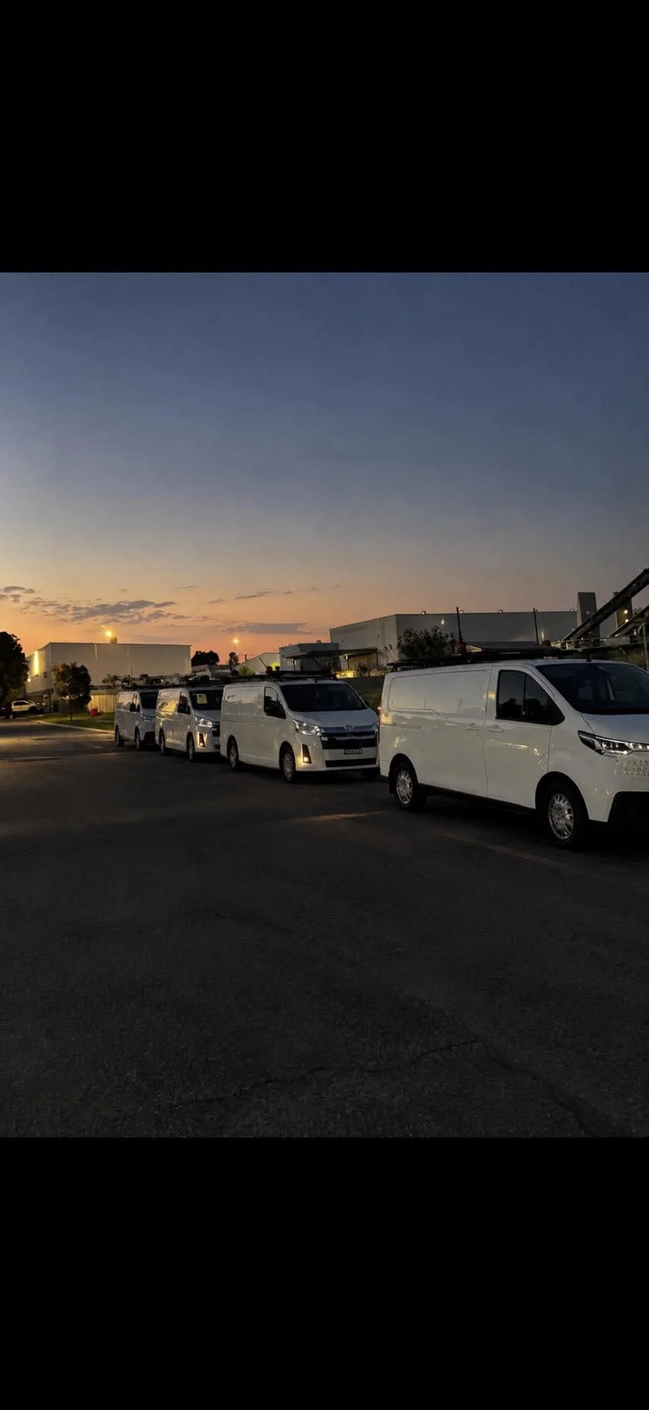 White work vans parked outside an industrial building at sunset
