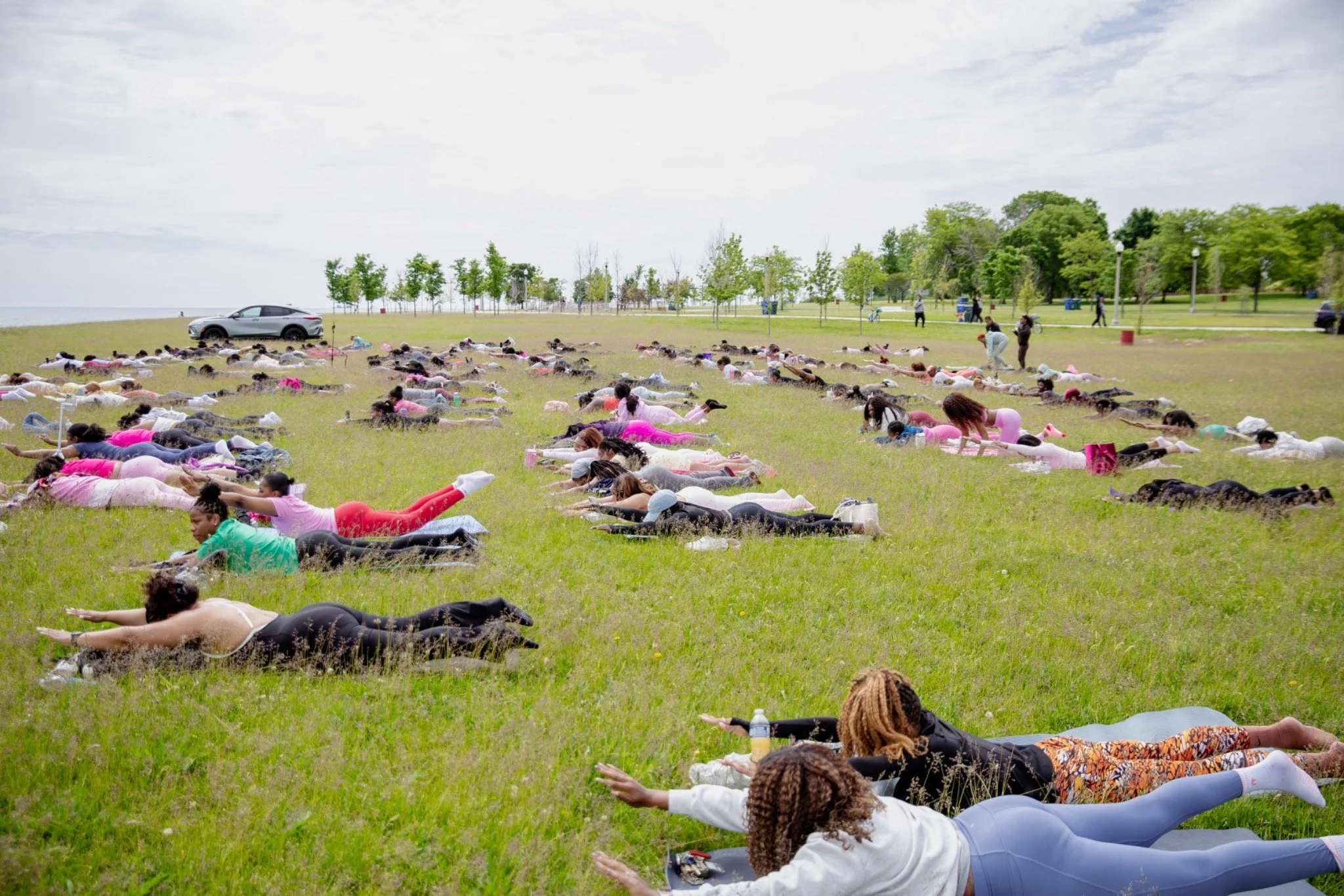 A large community Pilates class moving together outdoors beside Lake Michigan.