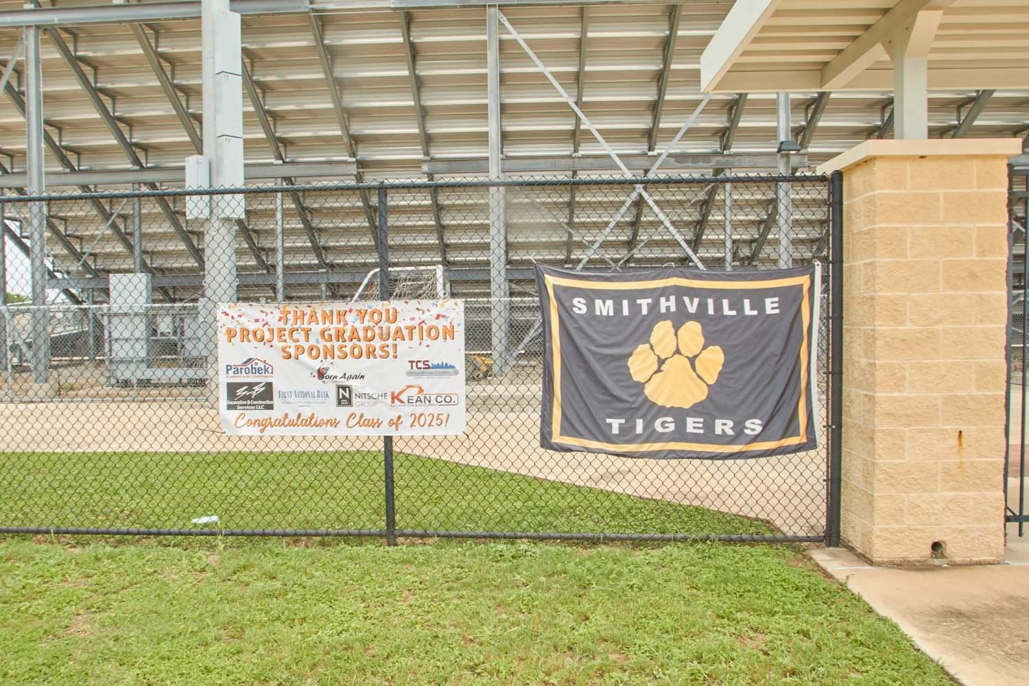 Black fence with two banners, one says 'Thank you Project Graduation Sponsors! Congratulations Class of 2015,' and the other has 'Smithville Tigers' with a tiger paw logo.