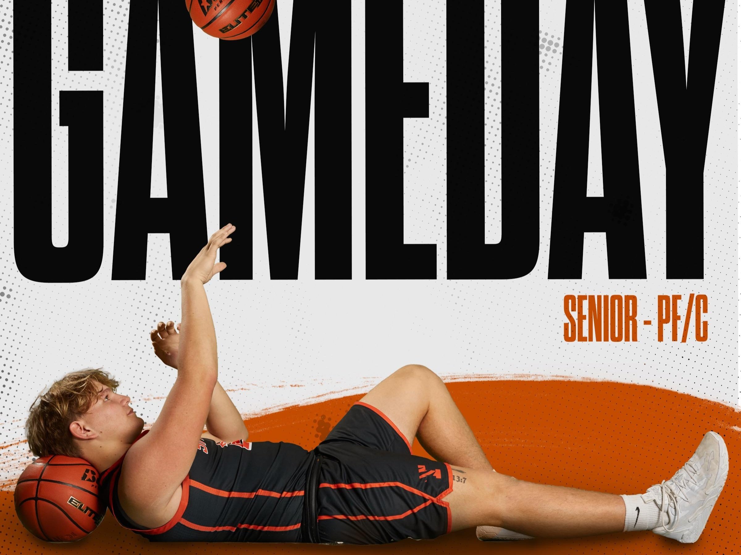 Young male basketball player lying on his side with a basketball under his head, reaching up towards the large text 'GAME DAY' on a sports-themed poster.