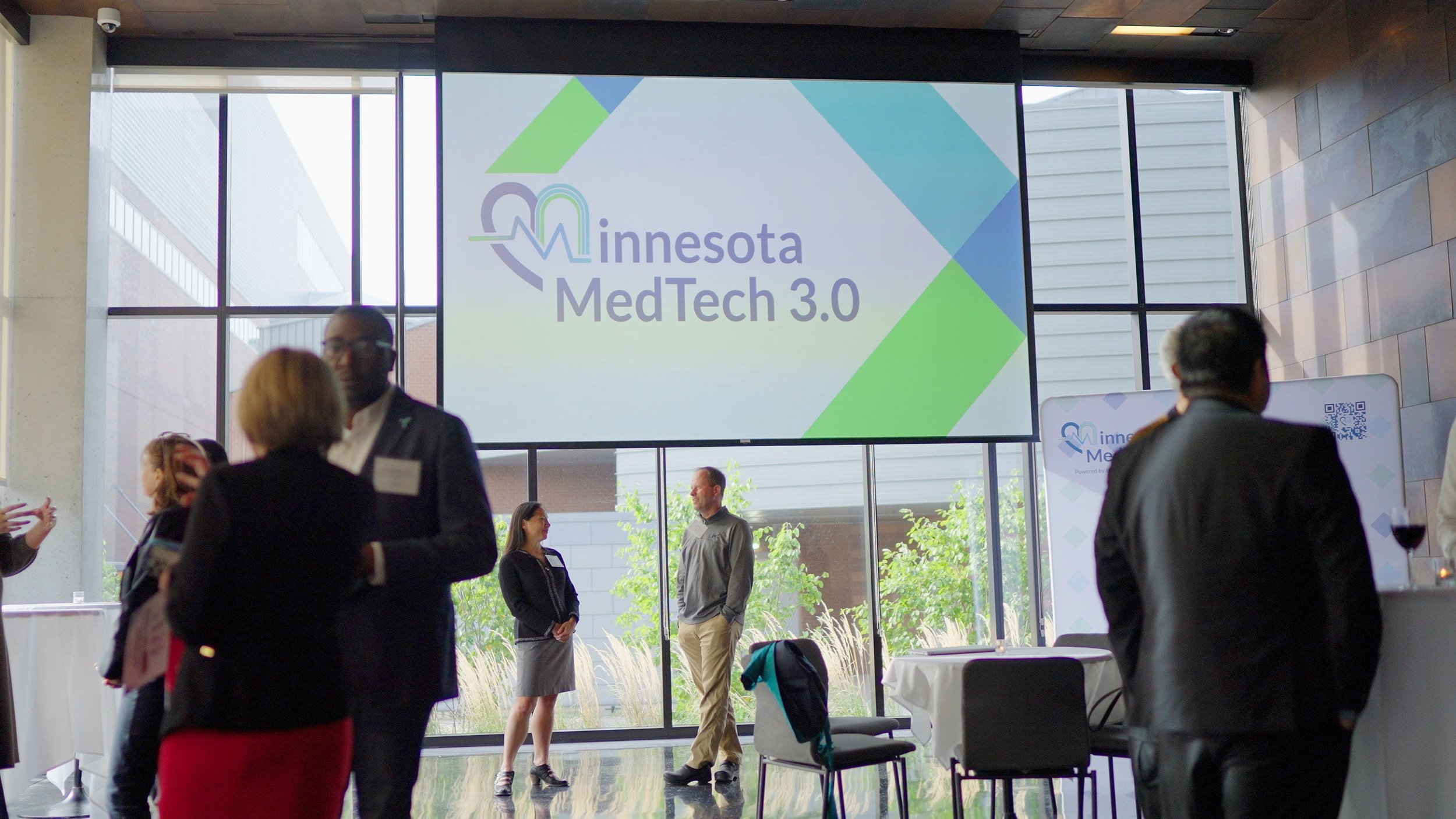 Attendees mingle at a Minnesota MedTech 3.0 event beneath a presentation screen displaying the event logo.