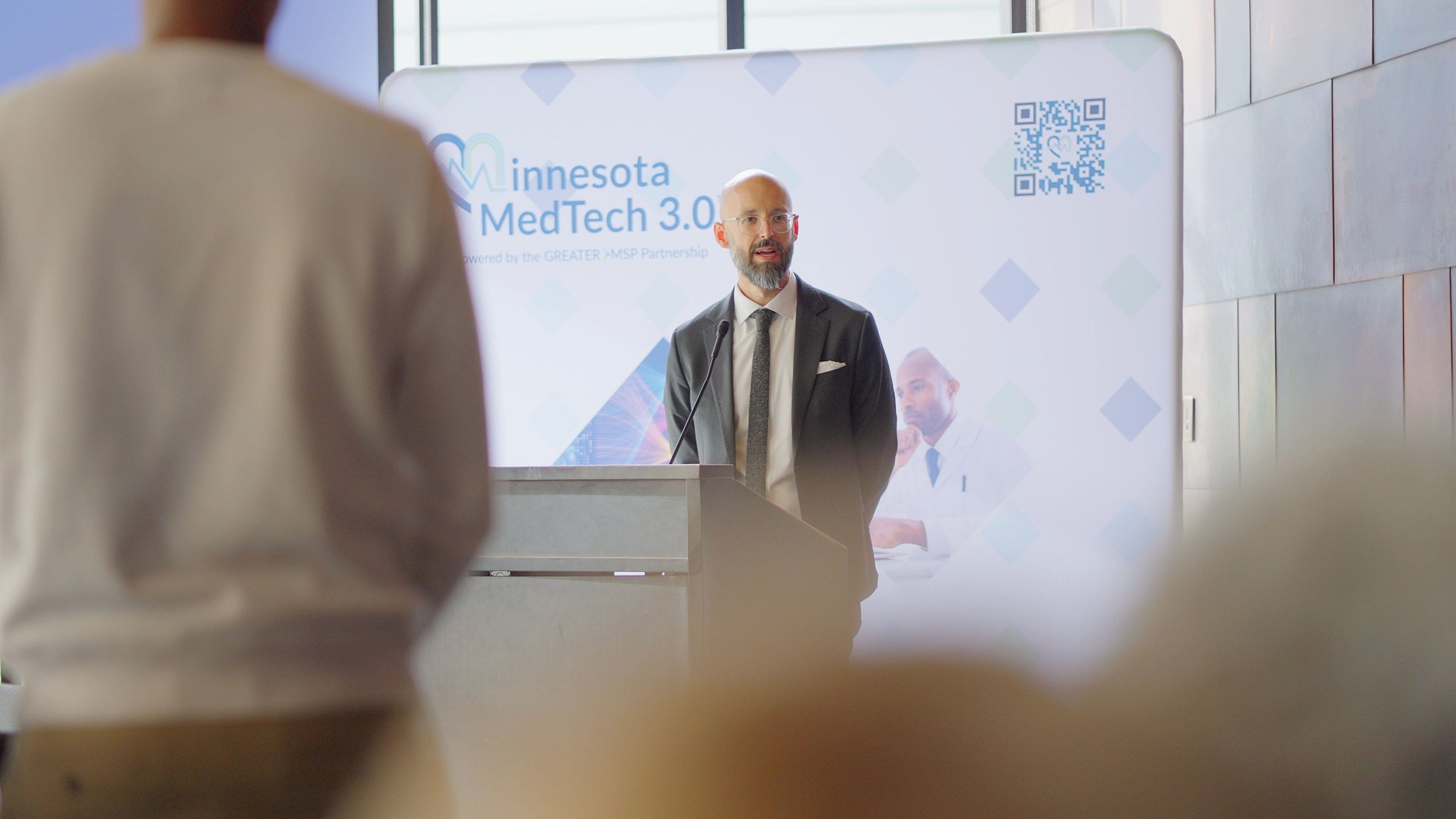 Man in a suit speaking at a podium during a Minnesota MedTech 3.0 event
