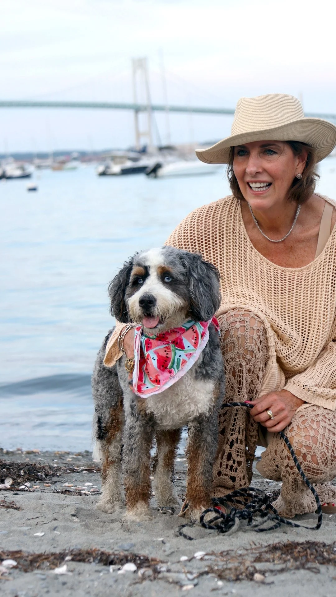 Lisa smiling on the beach with her Mini Bernedoodle Gracie