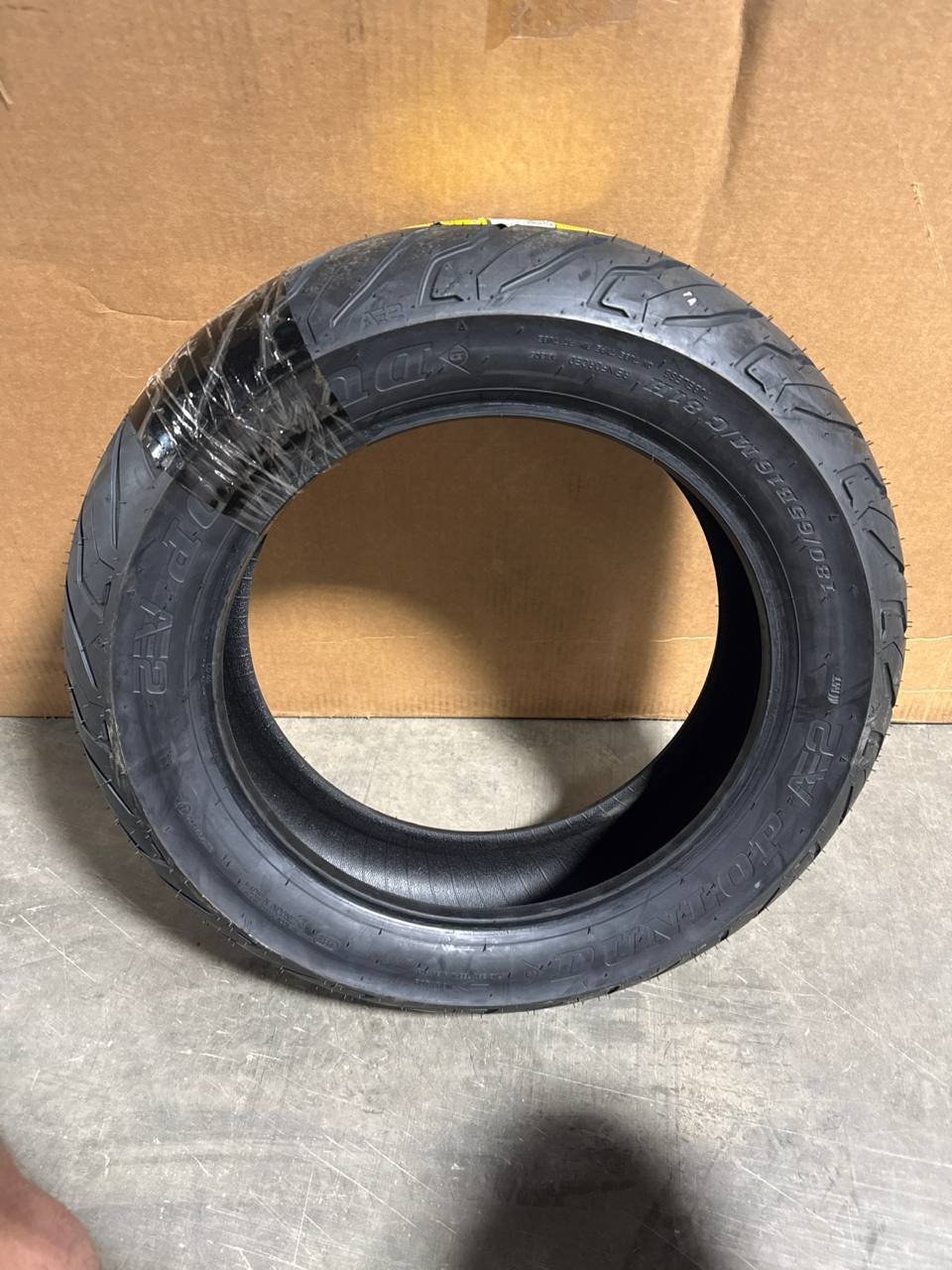 Actual Dunlop American Elite AE2 rear motorcycle tire standing upright in the warehouse, still partly wrapped