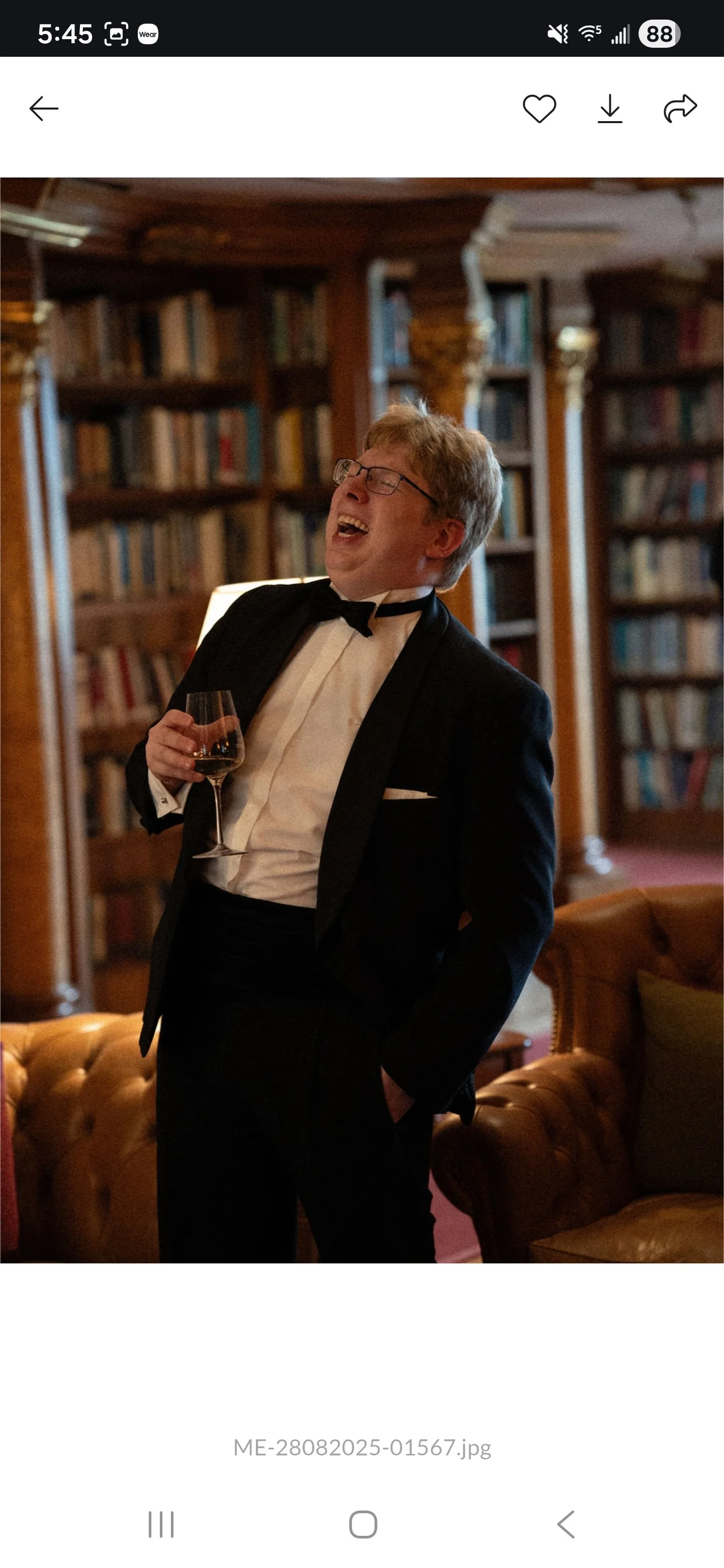 Smiling man in a tuxedo holding a wine glass in a cozy library lounge